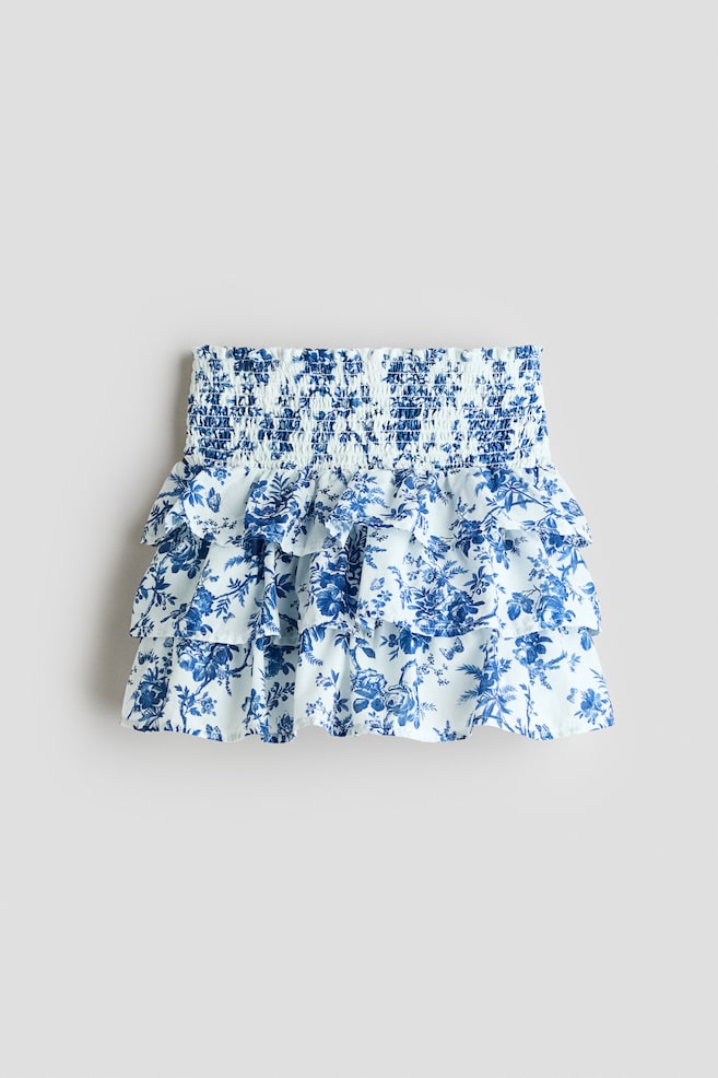 A skirt is facing front, featuring a shirred waistband and two tiers of ruffles, displaying a blue and white floral toile pattern. - 1