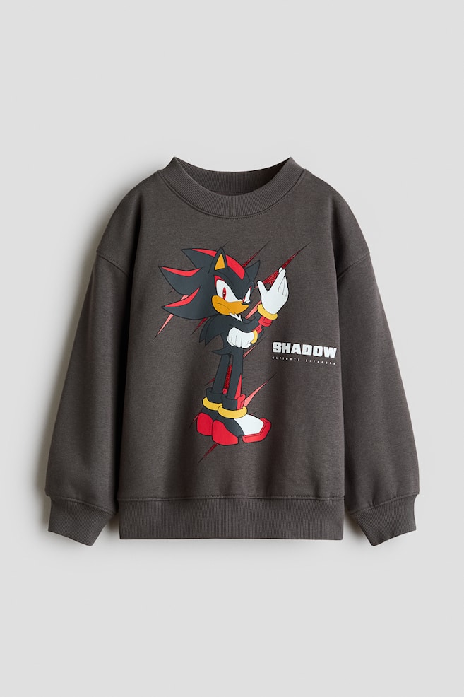Ciemnoszara, luÅºna bluza dresowa, widok z przodu, z nadrukiem przedstawiajÄcym postaÄ Shadow the Hedgehog oraz napisem âSHADOWâ na klatce piersiowej. Bluza ma okrÄgÅy dekolt wykoÅczony prÄÅ¼kowanym ÅciÄgaczem, obniÅ¼onÄ liniÄ ramion, dÅugie rÄkawy oraz prÄÅ¼kowane mankiety i dÃ³Å. - 1