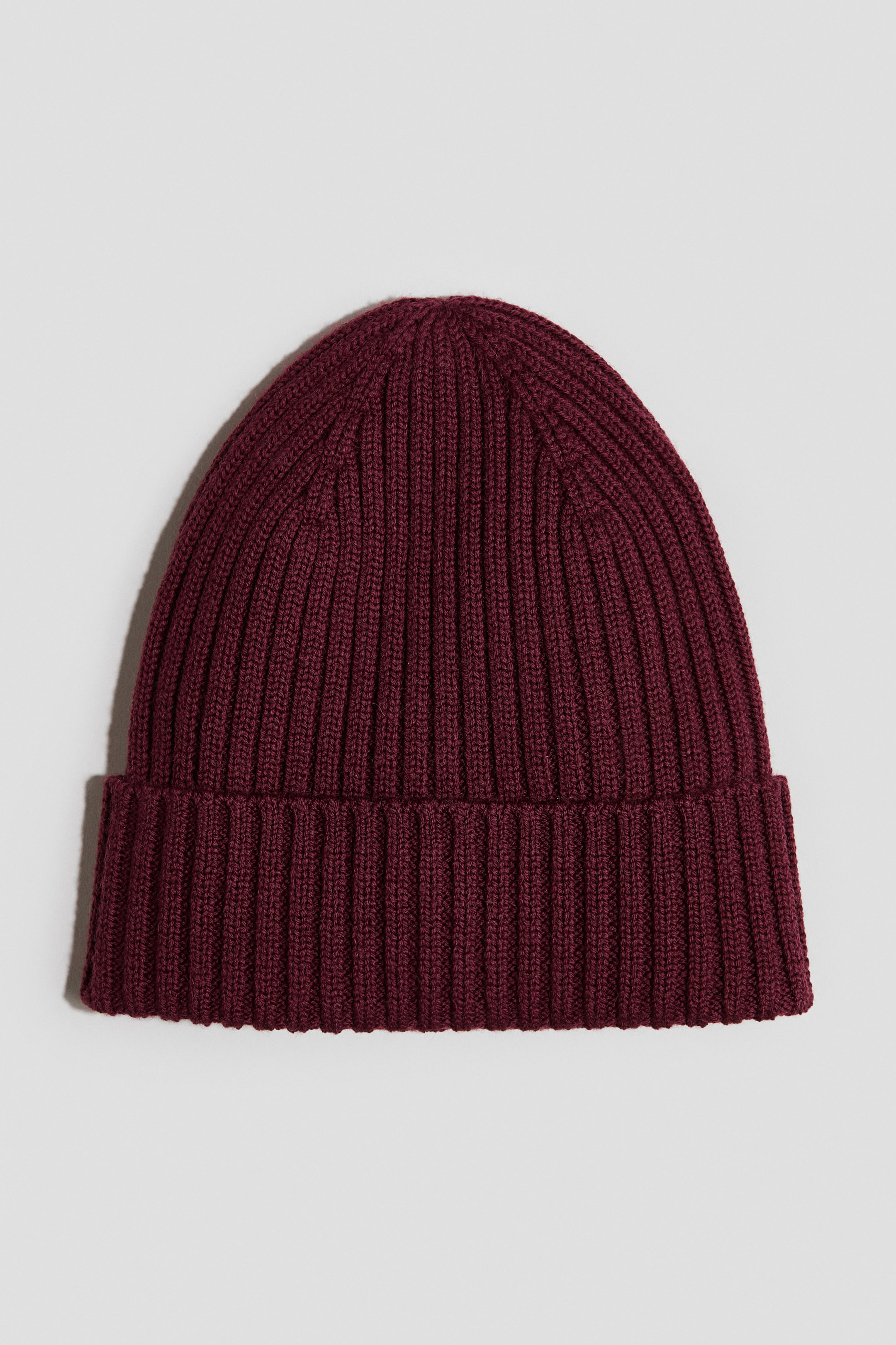Visa större bild: En vinröd ribbstickad beanie visas framifrån och har en bred, uppvikt fåll.