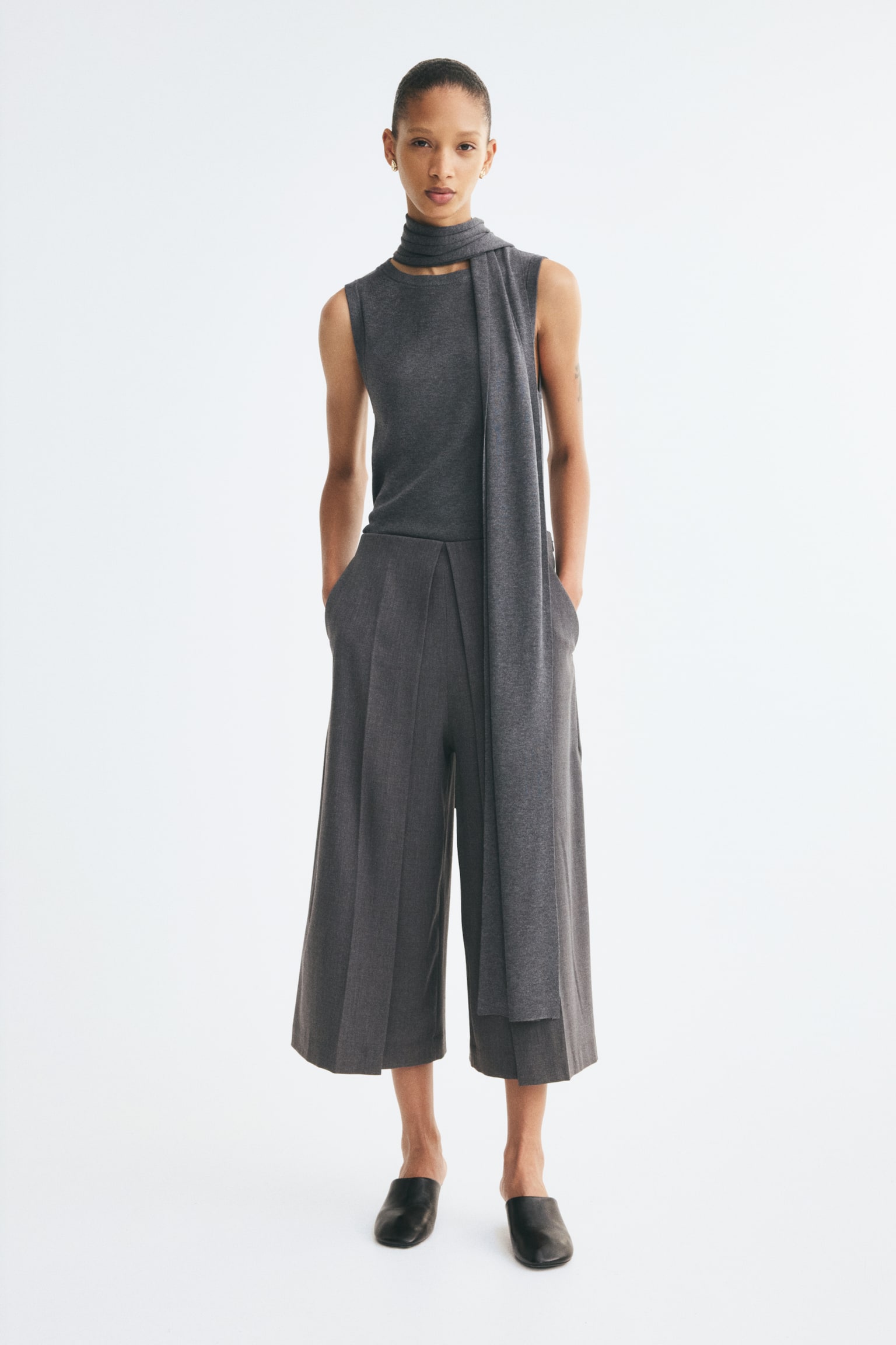 Dark grey woven wide-leg trousers are displayed from the front, featuring deep pleats down the centre of each leg and discreet side seam pockets. - 1