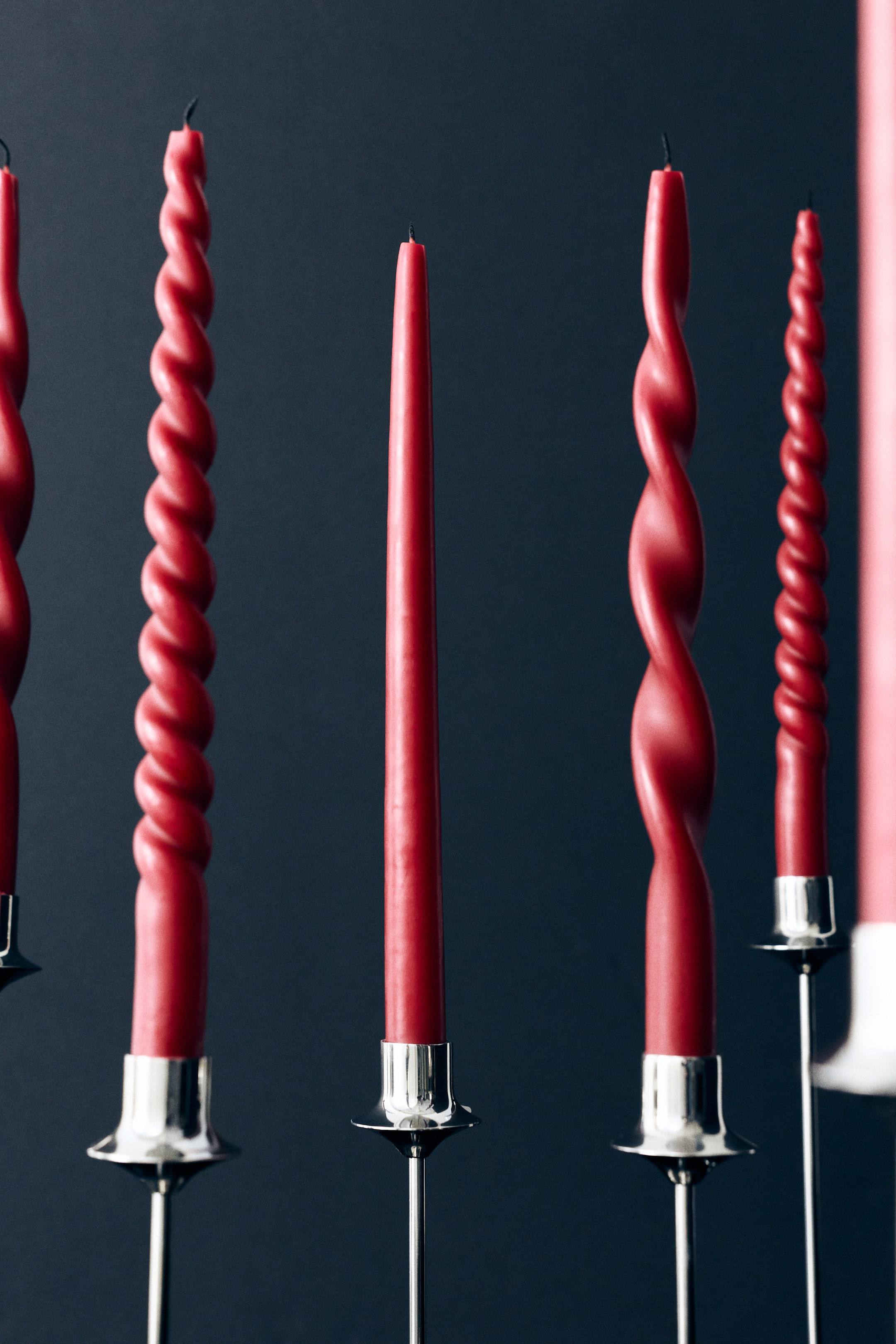 View larger image: Red taper candles stand upright in silver holders, showcasing three distinct shapes from the front: a smooth regular taper, a loose spiral, and a tight spiral. This view highlights the varied textures and structured designs of the candles.
