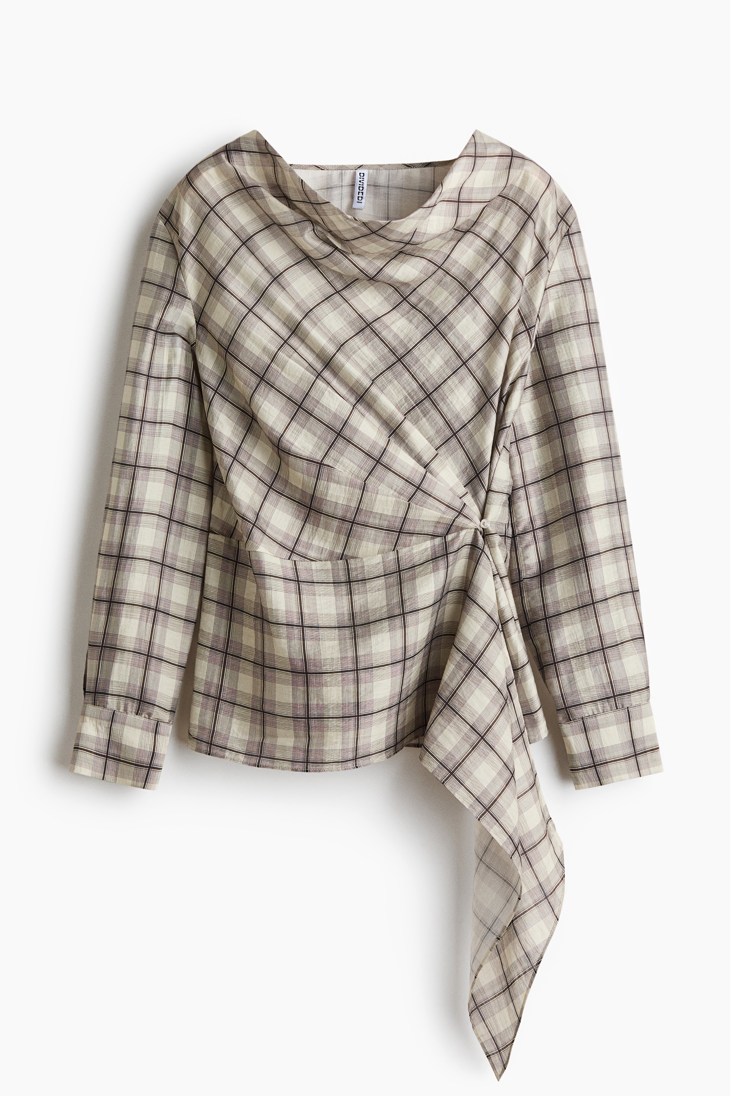 La modelo, en posiciÃ³n de cuclillas, lleva una blusa de cuadros con escote drapeado, frente con caÃ­da y un panel lateral largo y colgante. La blusa de manga larga se combina con shorts de mezclilla de lavado claro y deshilachados, asÃ­ como con una gorra de bÃ©isbol cafÃ©.