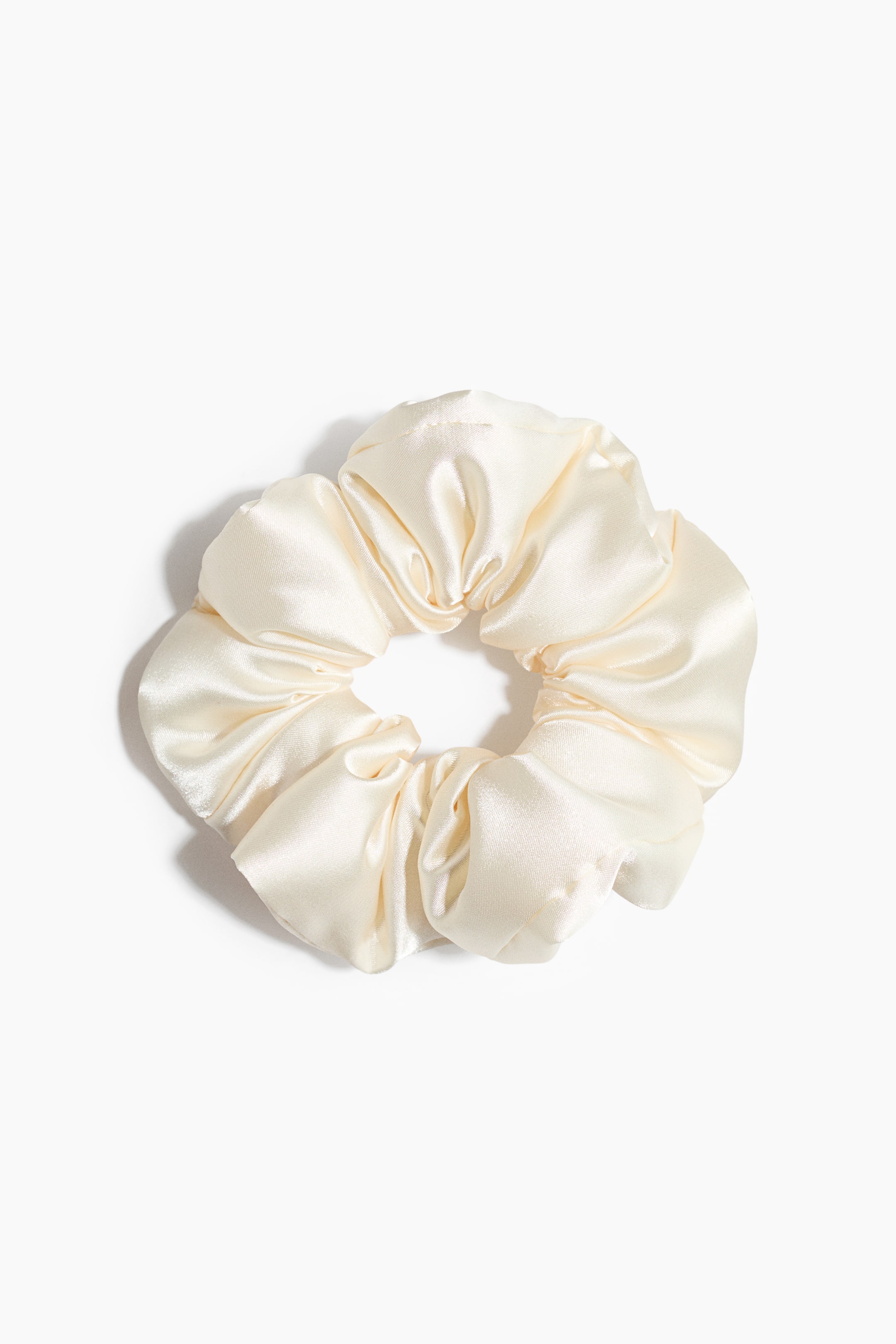 Se større billede: En cremefarvet scrunchie ligger fladt og viser sit rynkede, skinnende stof.