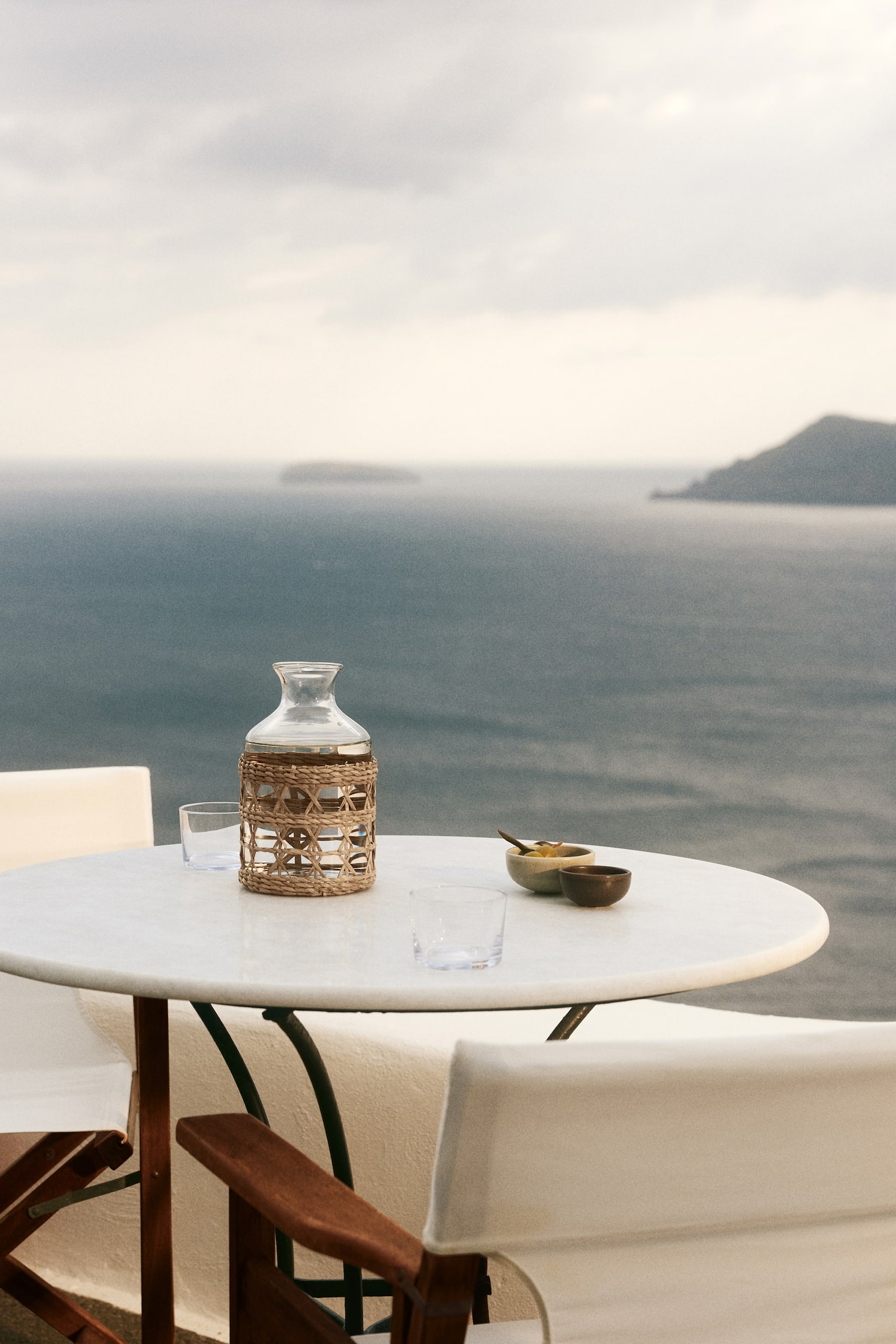 A clear glass carafe is filled with clear liquid and is encased in a woven natural fibre cover, which is displaying an open geometric pattern. - 1