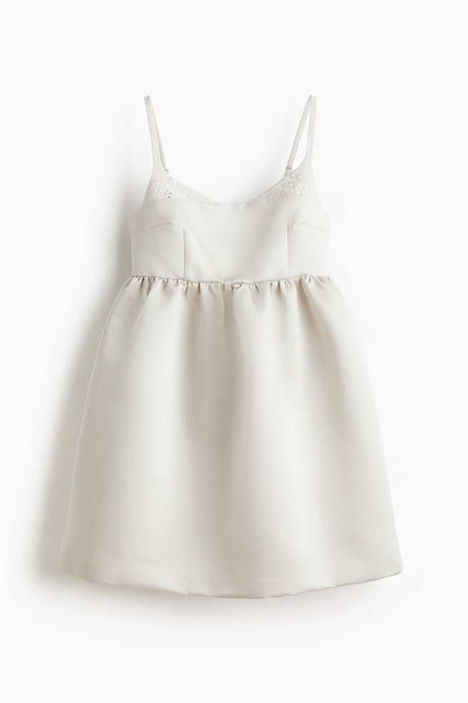 An off-white short dress is presenting FRONT, featuring delicate lace detailing along the neckline and thin spaghetti straps. The fitted bodice is transitioning into a gathered waistline, which is flowing into an A-line skirt with a subtle sheen. - 1