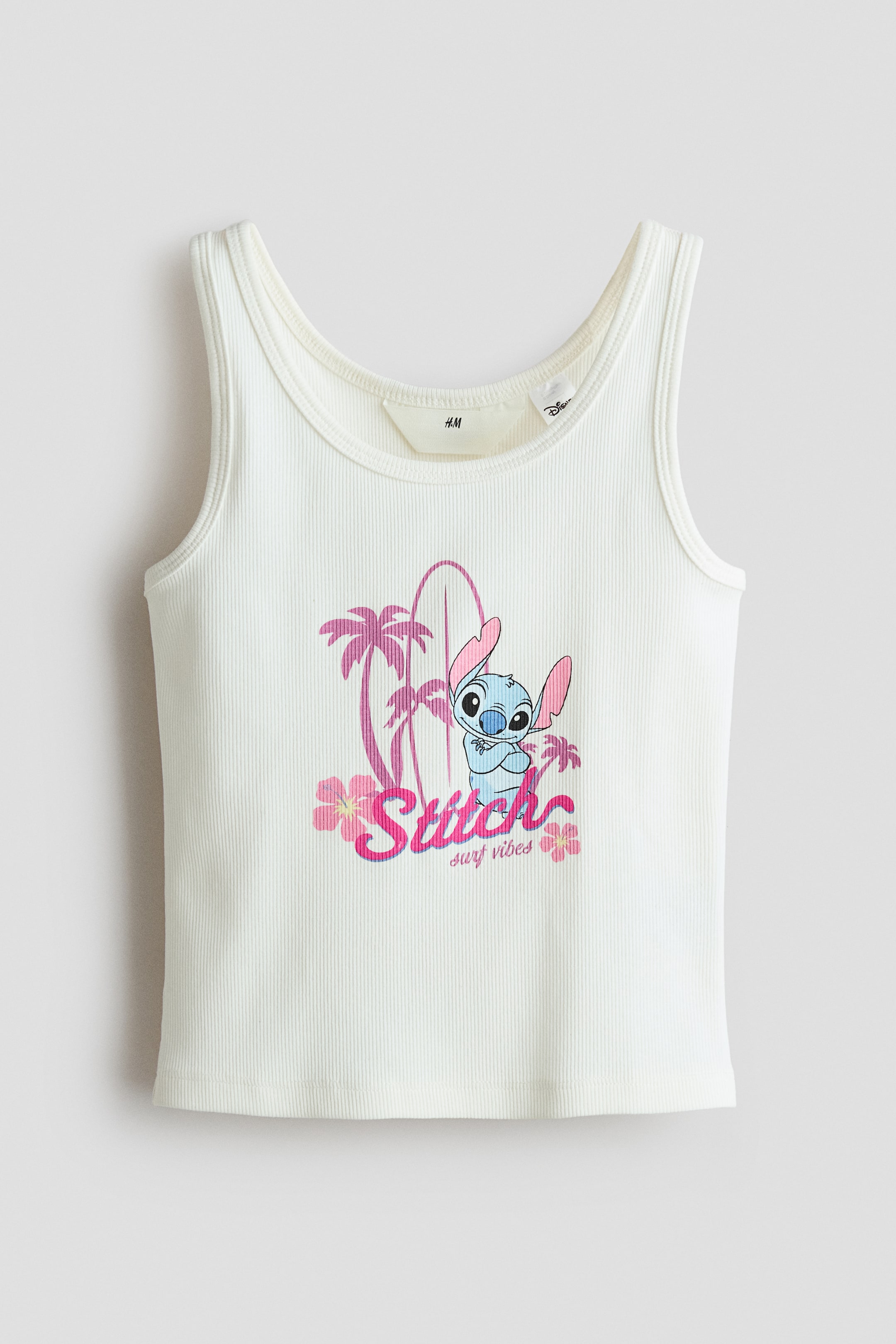View larger image: A white ribbed tank top showcasing a scoop neck and wide shoulder straps, features a central graphic on the front with the character Stitch, a surfboard, palm trees, and flowers, accompanied by the text 'Stitch surf vibes.'