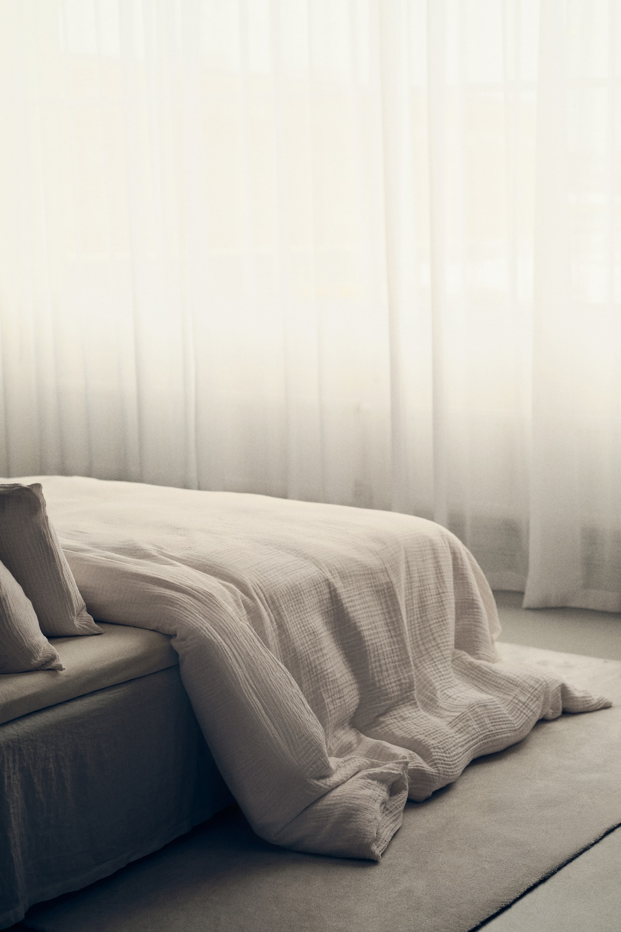 Zobrazit větší obrázek: Sada povlečení na dvojitou přikrývku, vyrobená z měkké bavlněné mušelínu, je rozprostřena přes postel. Světle zbarvené povlečení vykazuje zmačkanou texturu, přičemž dvě odpovídající povlaky na polštáře spočívají u čela.