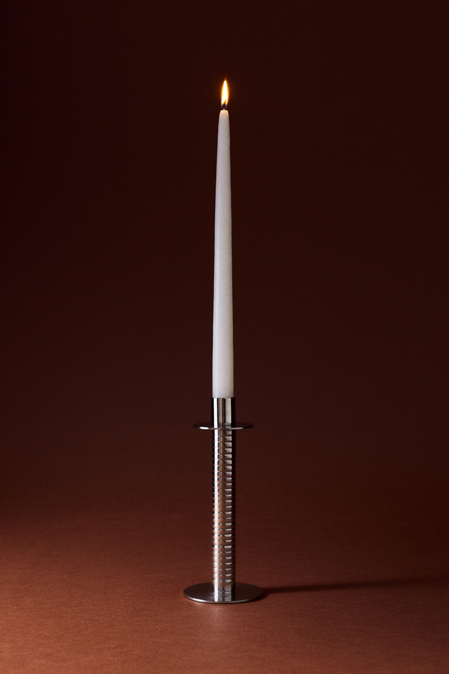 A silver-toned metal candlestick holds a white taper candle. The candlestick features a ribbed cylindrical stem, a flat circular base, and a circular drip tray. - 1