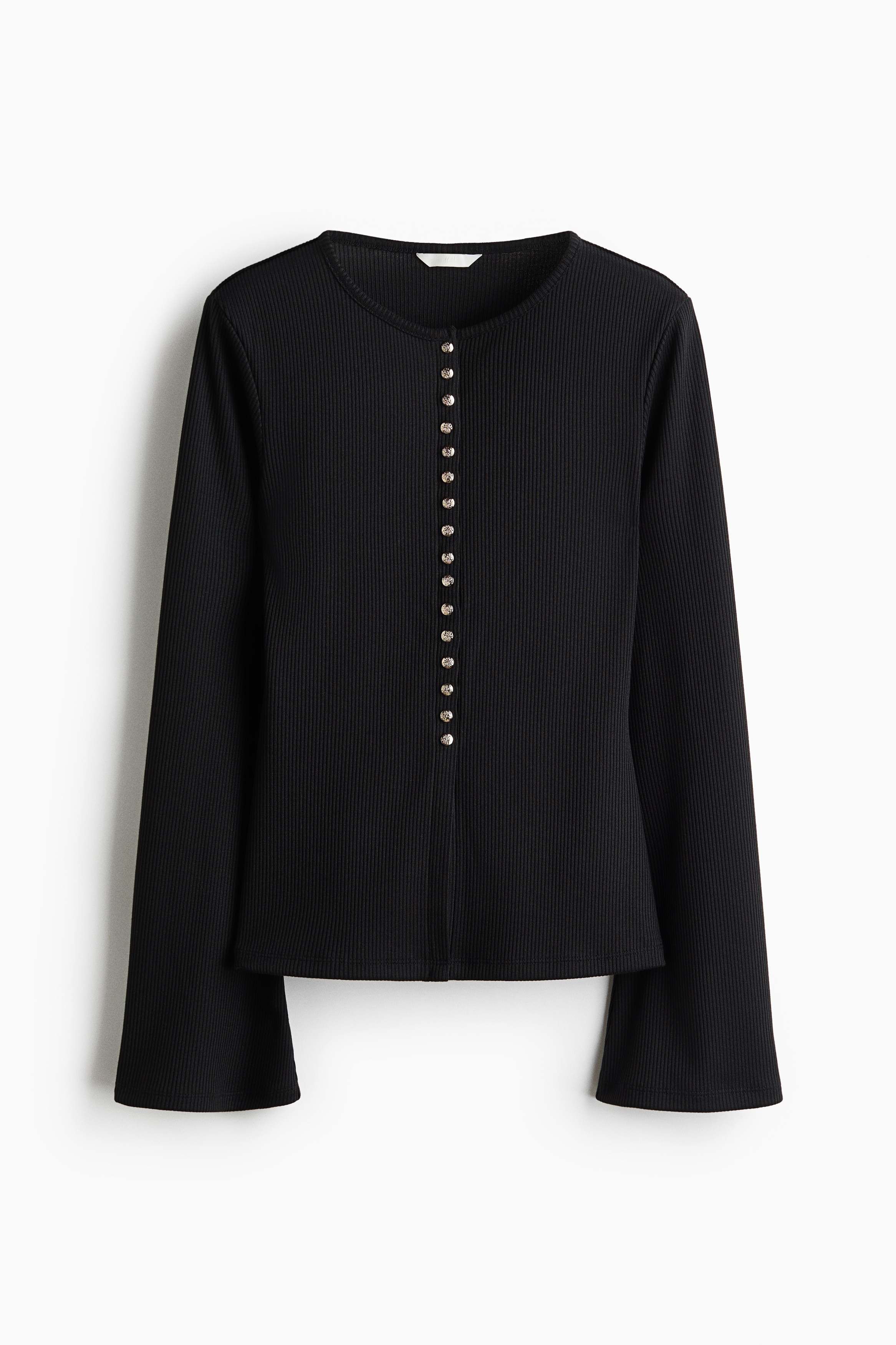 The model is wearing a black, fitted cardigan in rib-knit fabric, standing with arms crossed to highlight the long, flared sleeves. The cardigan features a round neckline and a row of metallic press studs down the front, and is paired with black trousers.