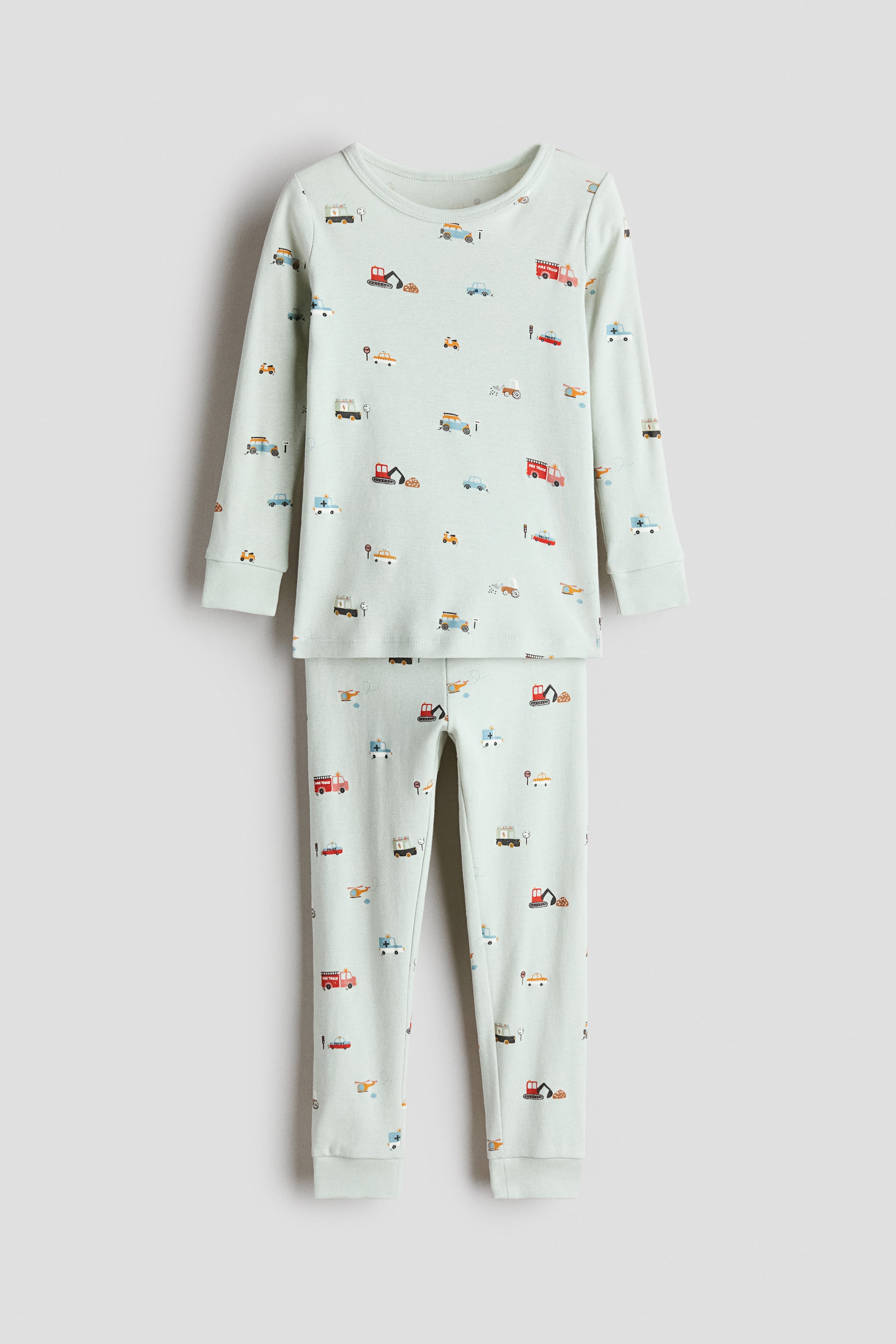 View larger image: This two-piece pajama set showcases a light green base color adorned with an allover print of various cartoon vehicles. The long-sleeved top is designed with a crew neck and ribbed cuffs, while the coordinating long pants also feature ribbed cuffs at the ankles.