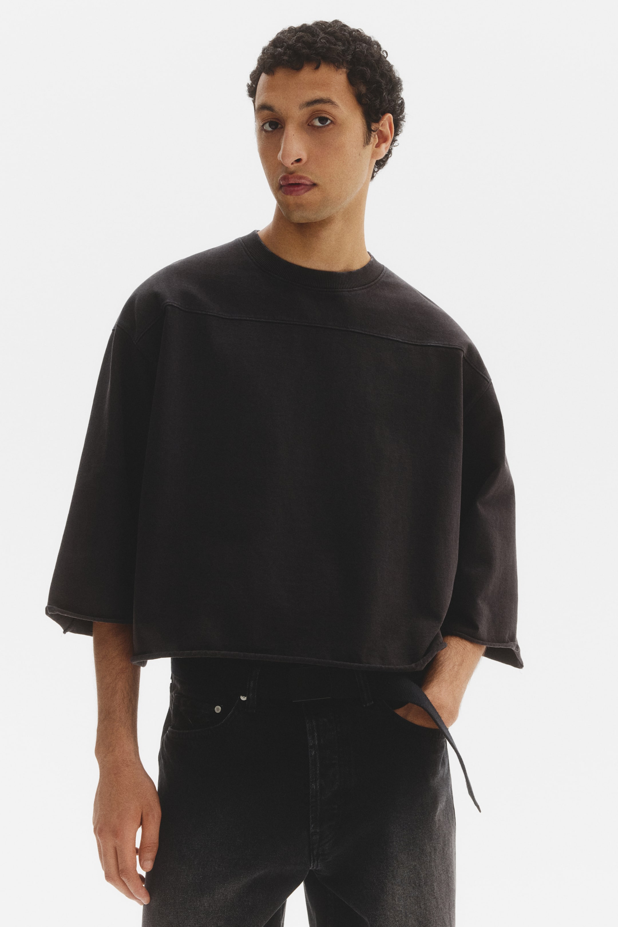 View larger image: Presenting a black cropped sweatshirt, displayed facing forward, showcasing an oversized fit with wide short sleeves and raw hems. It features a crew neck and noticeable horizontal seam details across the chest, with its raw bottom hem finishing above the waist.