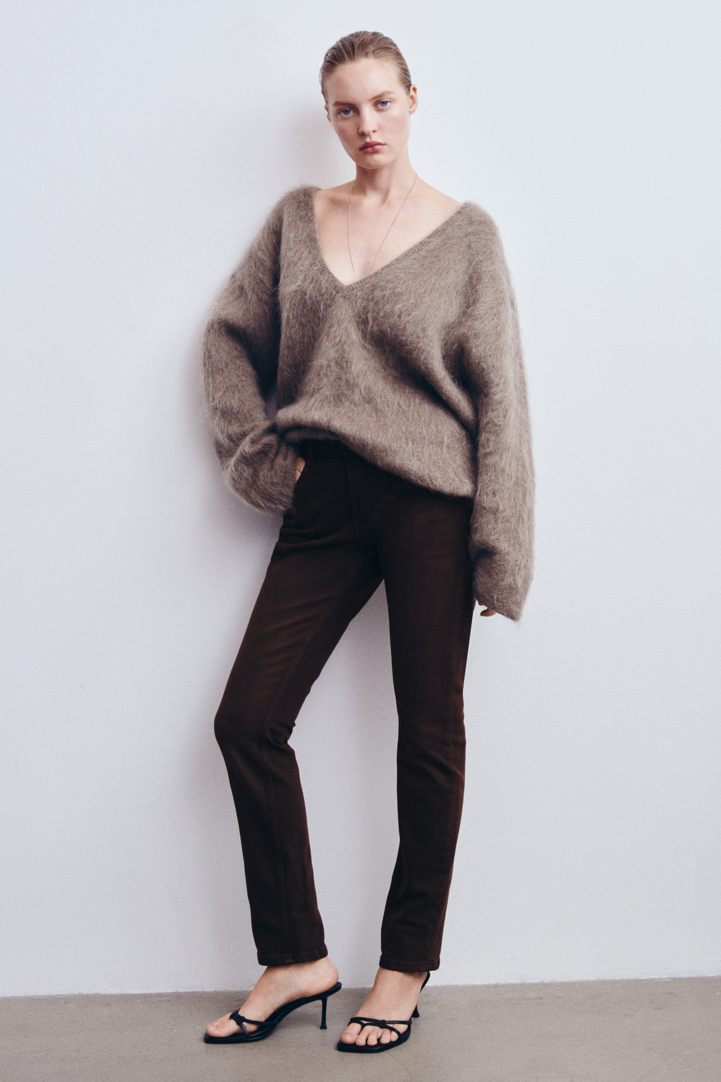 A pair of dark brown five-pocket jeans is shown from the front, featuring a regular-rise waist with belt loops and a button fastening. The jeans showcase a slim-fit leg with subtle fading on the thighs and classic silver-tone rivets on the pockets.