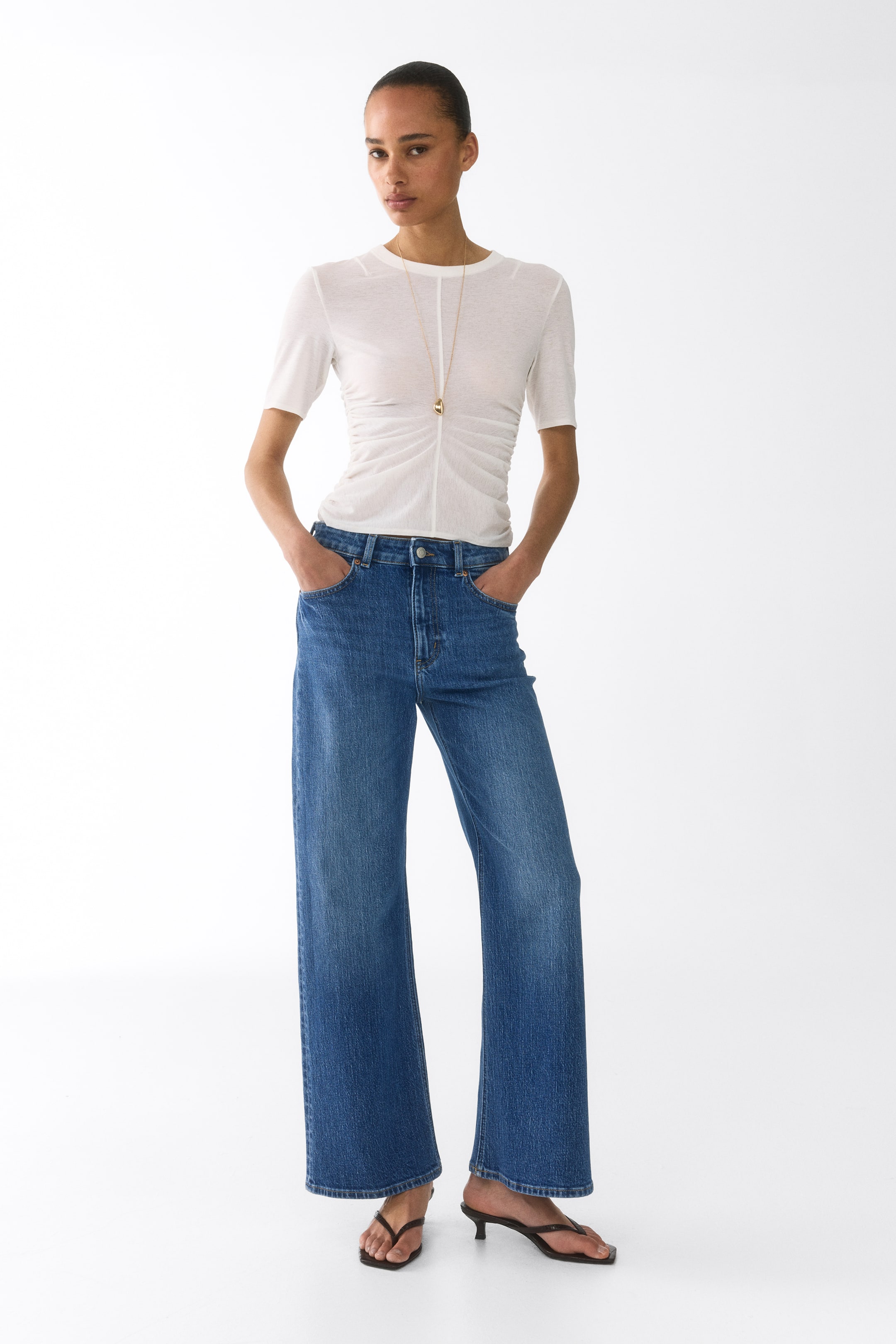 View larger image: Blue wide-leg jeans featuring a medium wash, a high-waisted design, and a button fastening, offering a relaxed fit. They are displayed worn, falling straight from the hips and highlighting their full length and wide-leg silhouette.