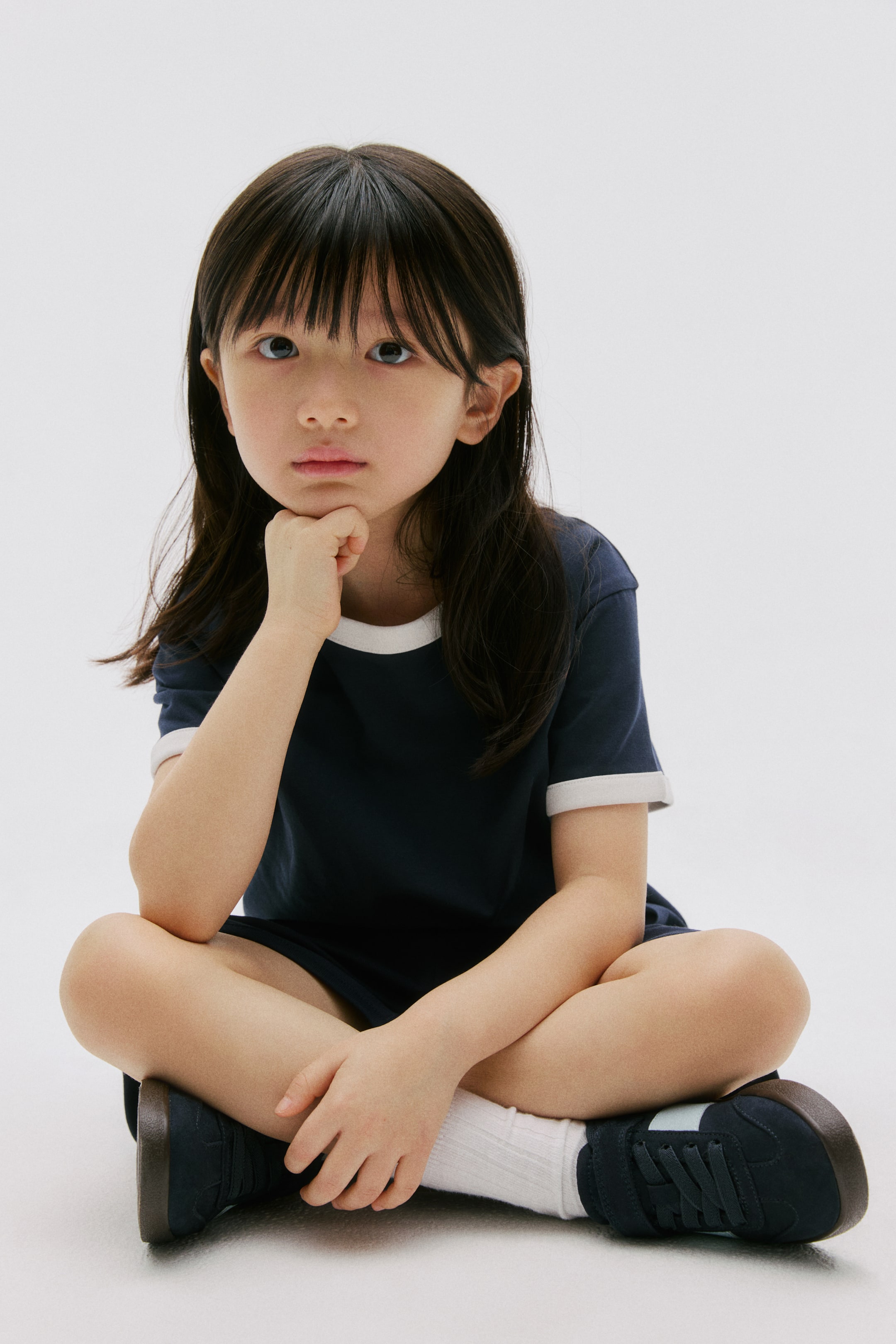 View larger image: A navy blue short-sleeved t-shirt is featuring white trim around its crew neck and sleeve cuffs, and it is being worn with matching navy blue shorts.