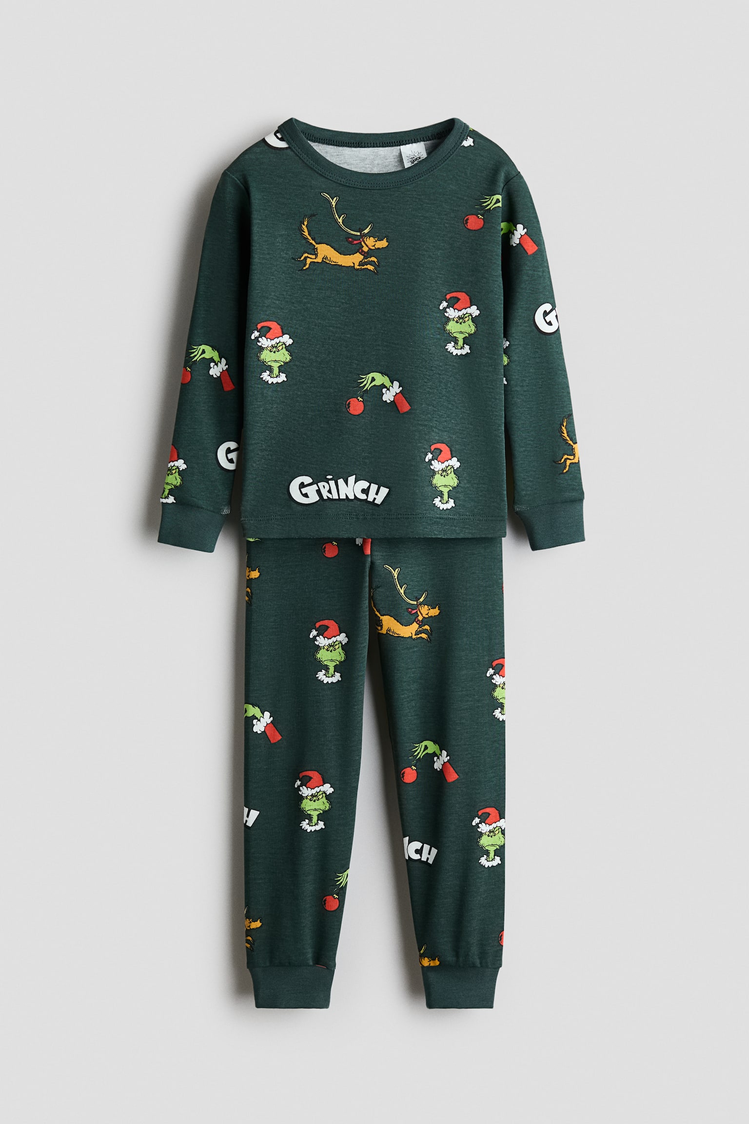 A dark green cotton jersey pyjama set is displaying a front view of a long-sleeve top and matching pants featuring an all-over print of The Grinch and Max. The top is showing a round neckline and ribbed cuffs, while the matching pants are featuring an elasticated waistband and ribbed ankle cuffs.