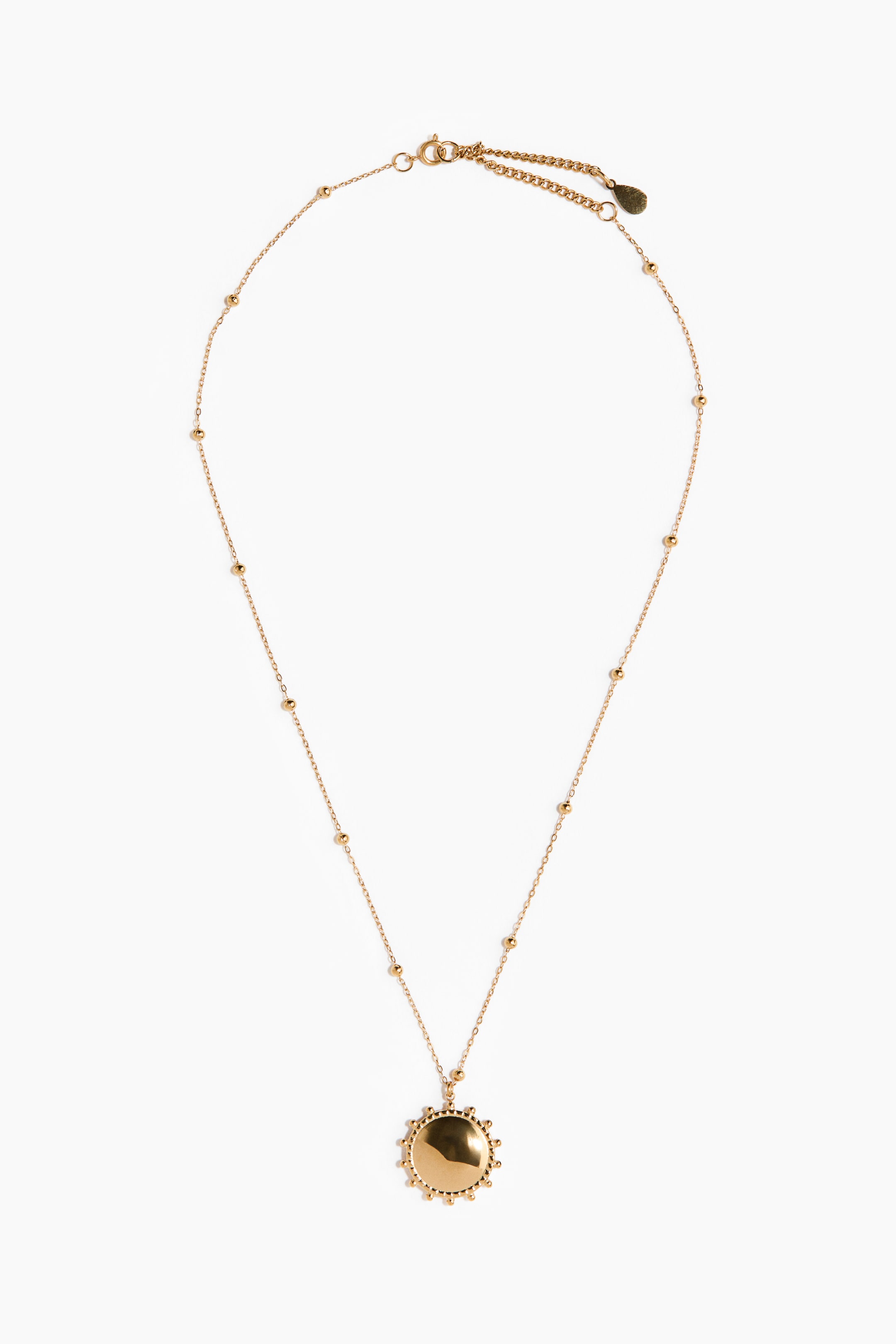 Grotere afbeelding bekijken: Een goudkleurige ketting hangt verticaal, met een delicate ketting voorzien van kleine, ronde kralen die langs de lengte zijn verdeeld. Aan de onderkant is een ronde, goudkleurige hanger bevestigd met een gladde kern en een rand van kralen, naar voren gericht, terwijl een karabijnsluiting en een verlengketting zichtbaar zijn aan de bovenkant.