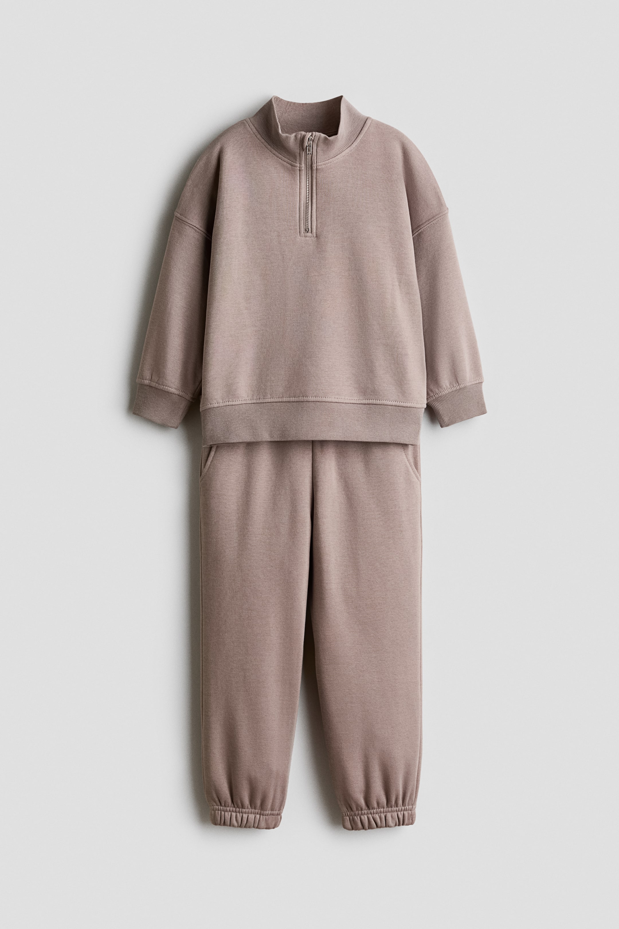 View larger image: A two-piece taupe loungewear set, shown from the front, featuring a half-zip sweatshirt with a stand-up collar, a silver-toned zip, ribbed cuffs and a ribbed hem. The coordinating sweatpants feature side pockets and gathered elasticated ankles.