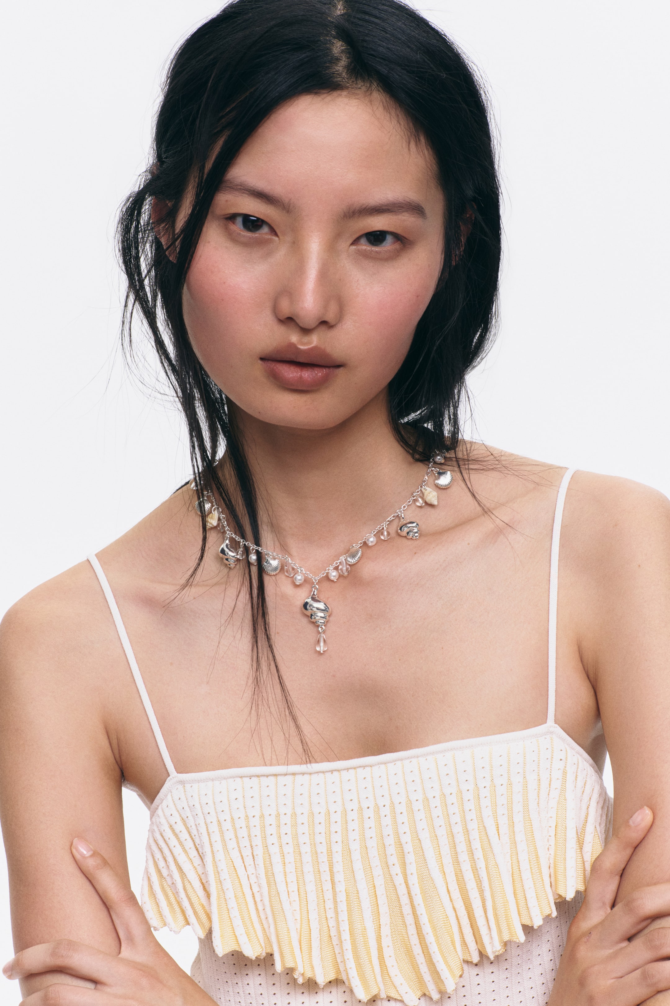 Ver imagen más grande: Un collar de tono plateado exhibe varios dijes con forma de concha y pequeñas cuentas redondas e iridiscentes. Un dije de concha más grande y en espiral con un colgante transparente en forma de lágrima cuelga en el centro.