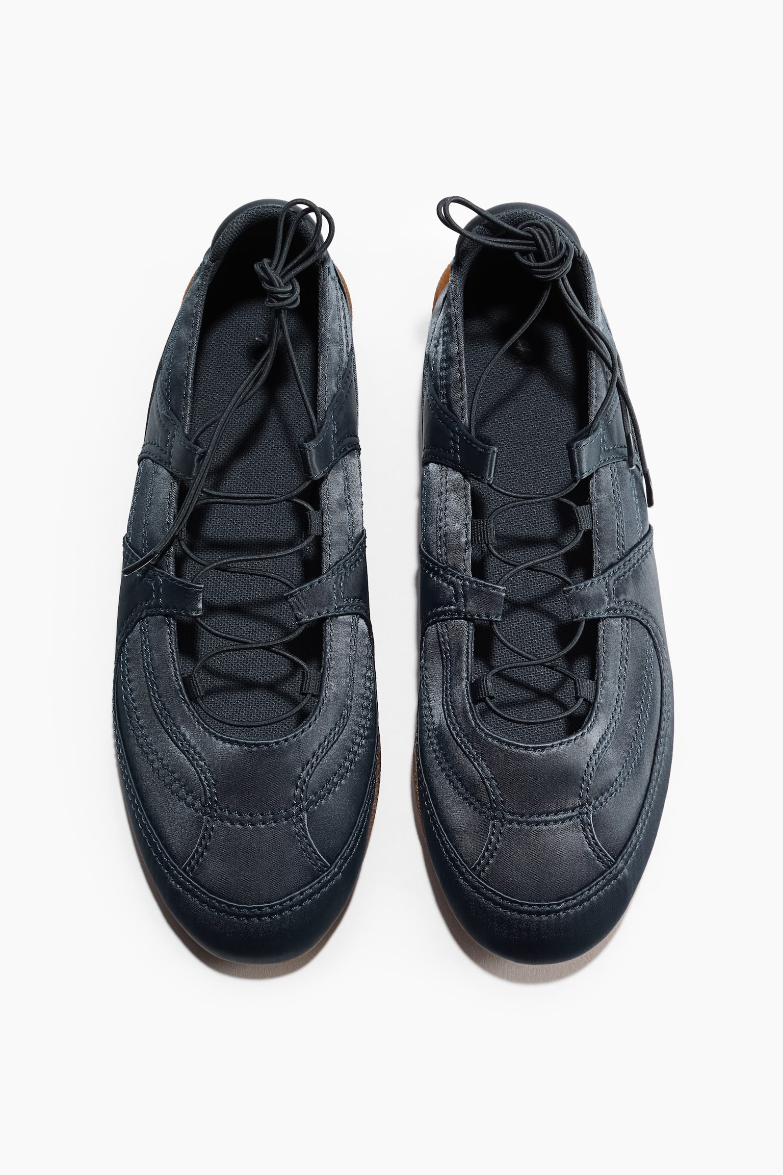 Une paire de chaussures décontractées bleu foncé est présentée en vue de dessus, orientée vers l'avant. Chaque chaussure arbore une tige cousue avec des lacets élastiques noués au sommet, et un bord de semelle fin marron est visible. - 1