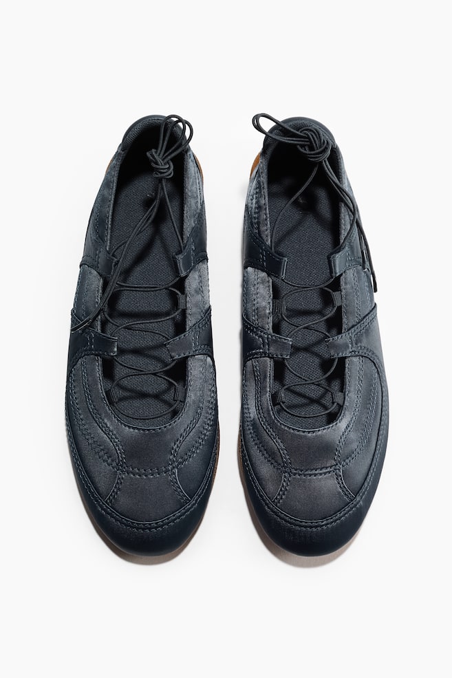 A pair of dark blue casual shoes is displayed from a top-down perspective, facing forward. Each shoe showcases a stitched upper with elastic laces tied in a knot at the top, and a slim brown sole edge is visible. - 1