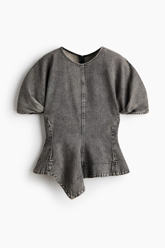 Un haut en denim gris foncé délavé se présente à l'avant, mettant en valeur un col rond, des manches courtes et larges, ainsi qu'une couture verticale centrale. Les coutures latérales incurvées façonnent la taille ajustée, qui s'évase vers un ourlet asymétrique à bord brut avec un détail pointu sur la gauche. - 1