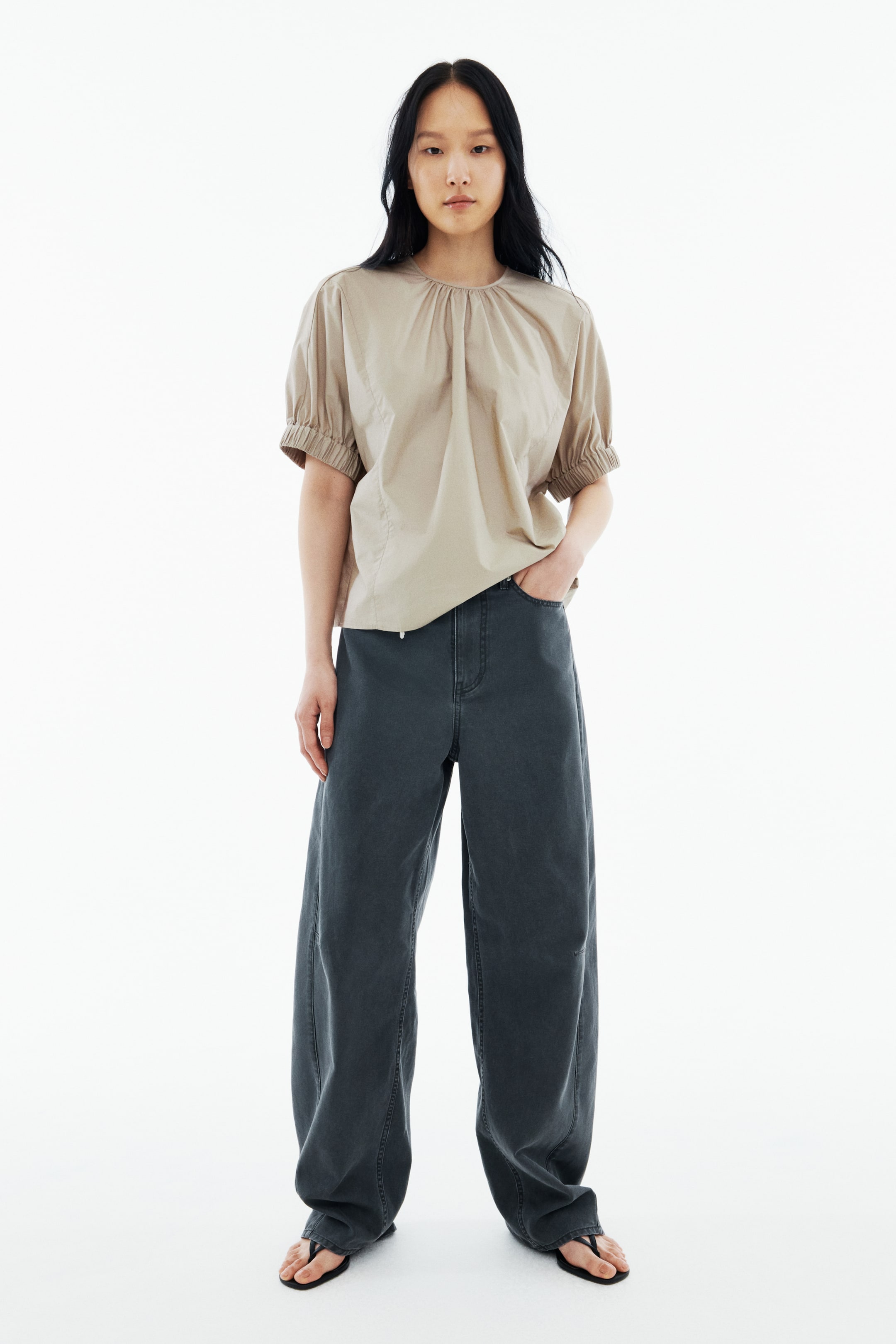 View larger image: A beige short-sleeved top features a gathered round neck and elasticated puffed sleeves. It's paired with dark grey wide-leg pants, showcasing prominent front seams and a loose fit.