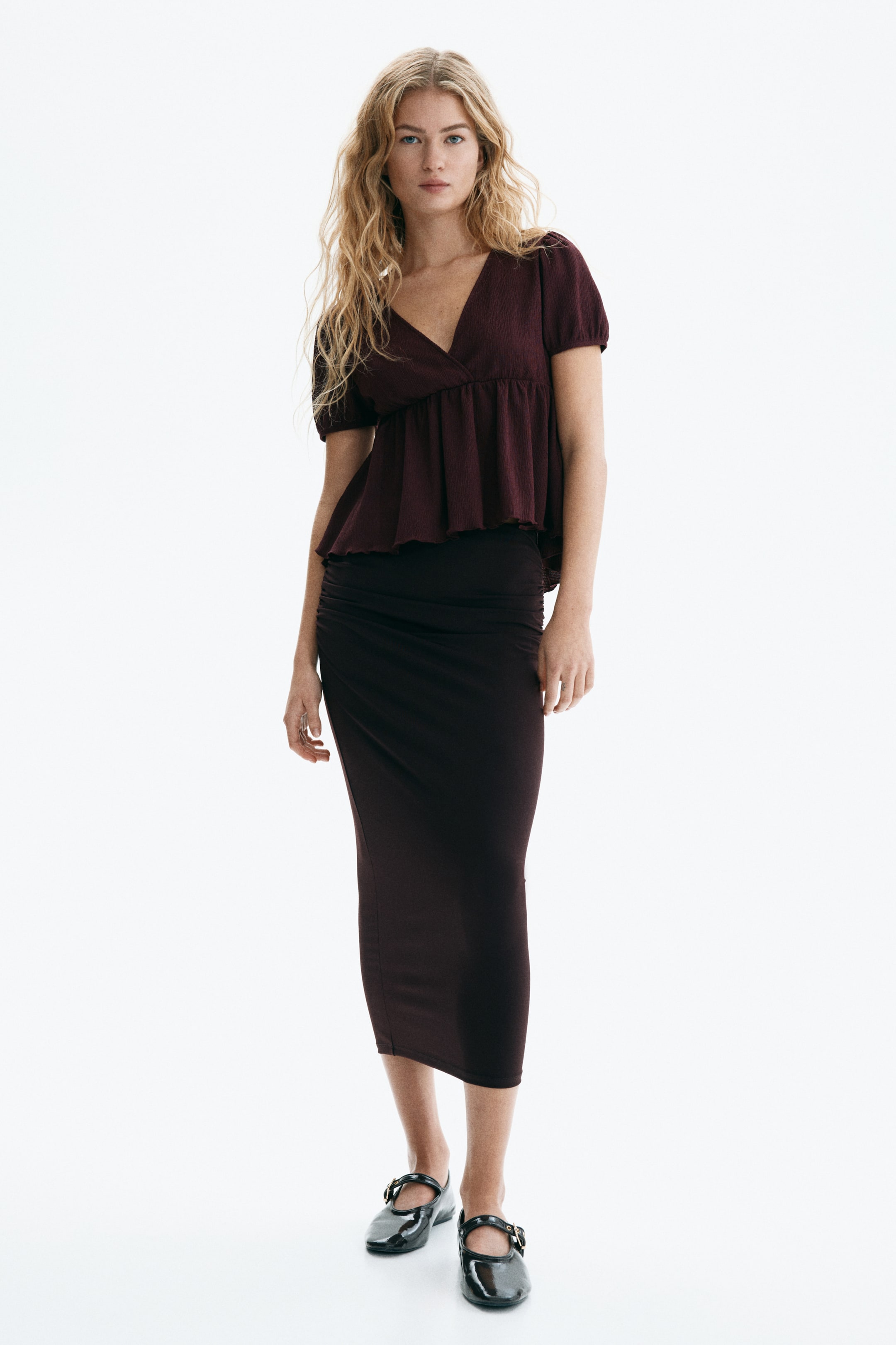 View larger image: Burgundy short-sleeve top featuring a V-neckline, wrap-style bodice, and textured fabric, with gathered puff sleeves and a flared peplum hem.