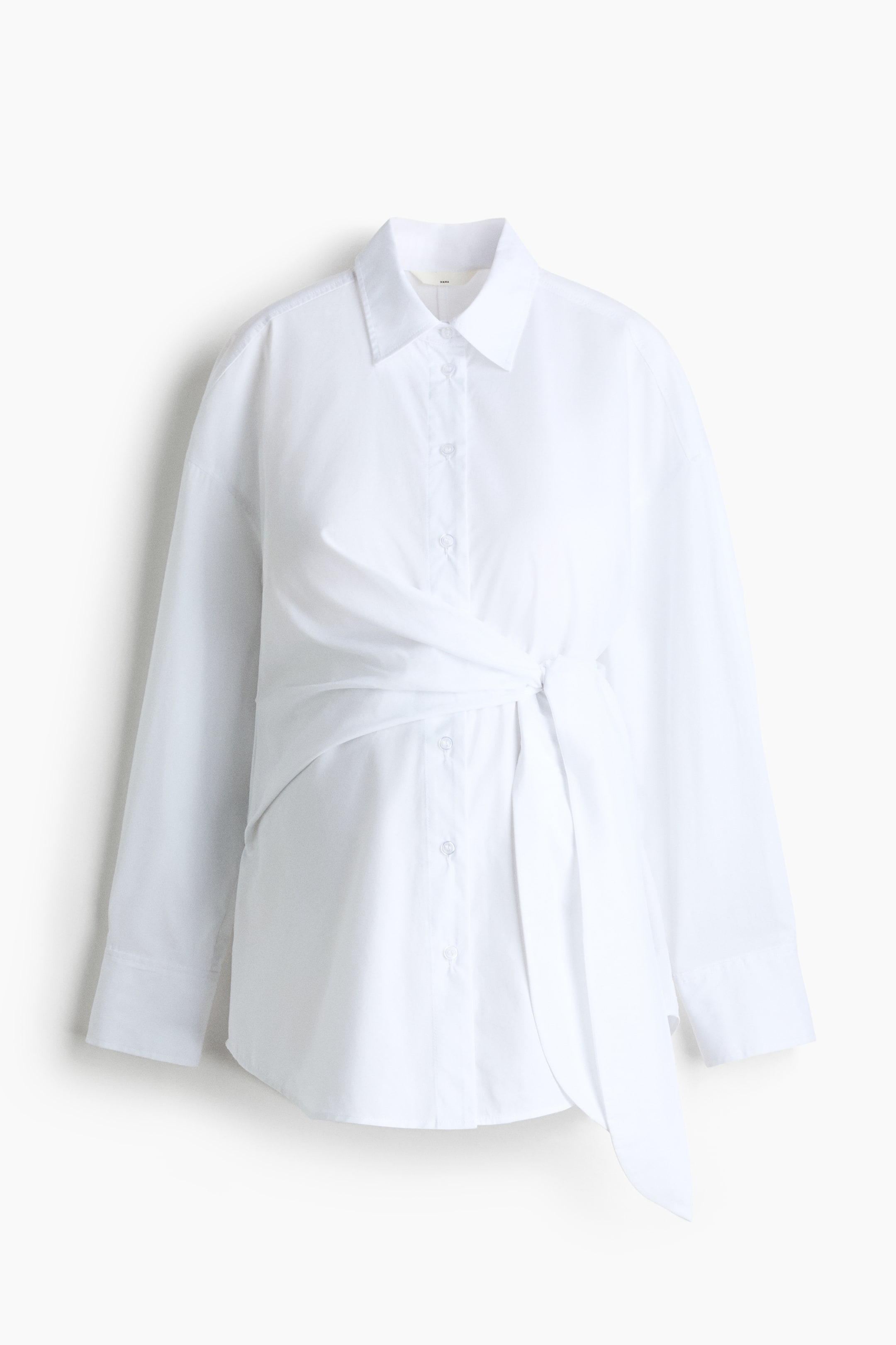 View larger image: This white shirt, crafted from a cotton weave, is displayed from the front, highlighting its collar, button-down front, dropped shoulders, and long sleeves with buttoned cuffs. A tie detail creates a draped effect across the front, and a subtly rounded hem is visible.