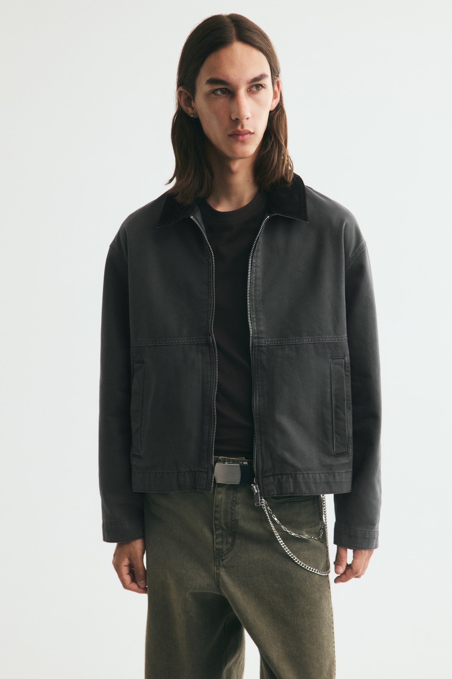 A short dark grey cotton canvas workwear jacket is shown from the front, featuring a contrasting black corduroy spread collar. A silver-tone zip runs down the centre front, with two rectangular welt pockets visible on the lower front, and long sleeves extending to a straight-cut hem. - 1