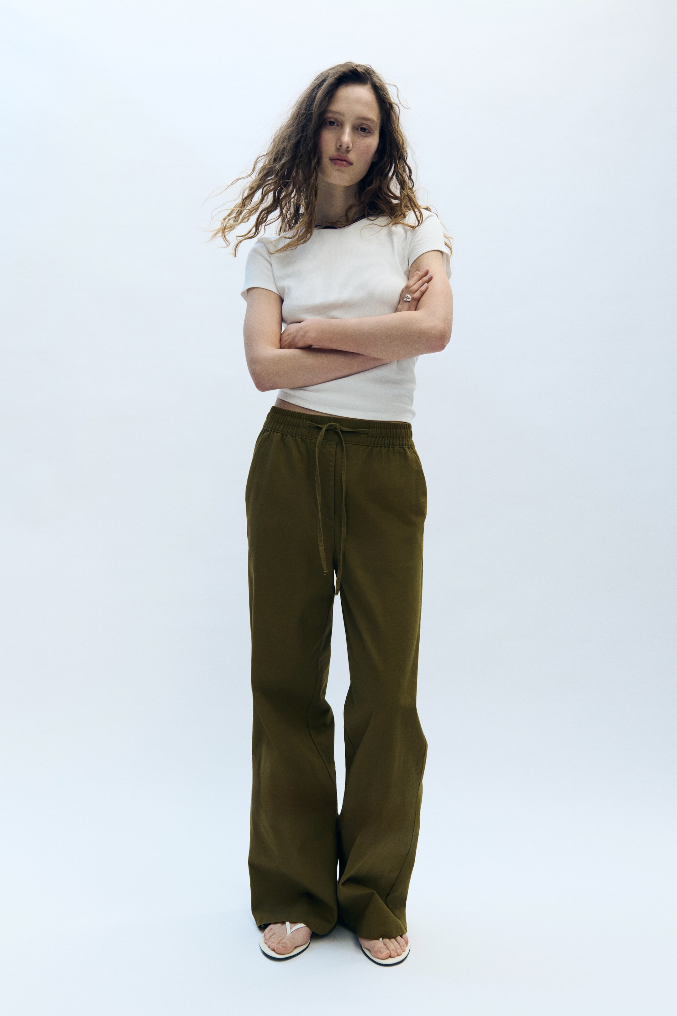 View larger image: Olive green wide-leg pants feature a relaxed fit with a visible drawstring at the elastic waistband. They extend to the floor, creating a slight pooling effect at the ankles.