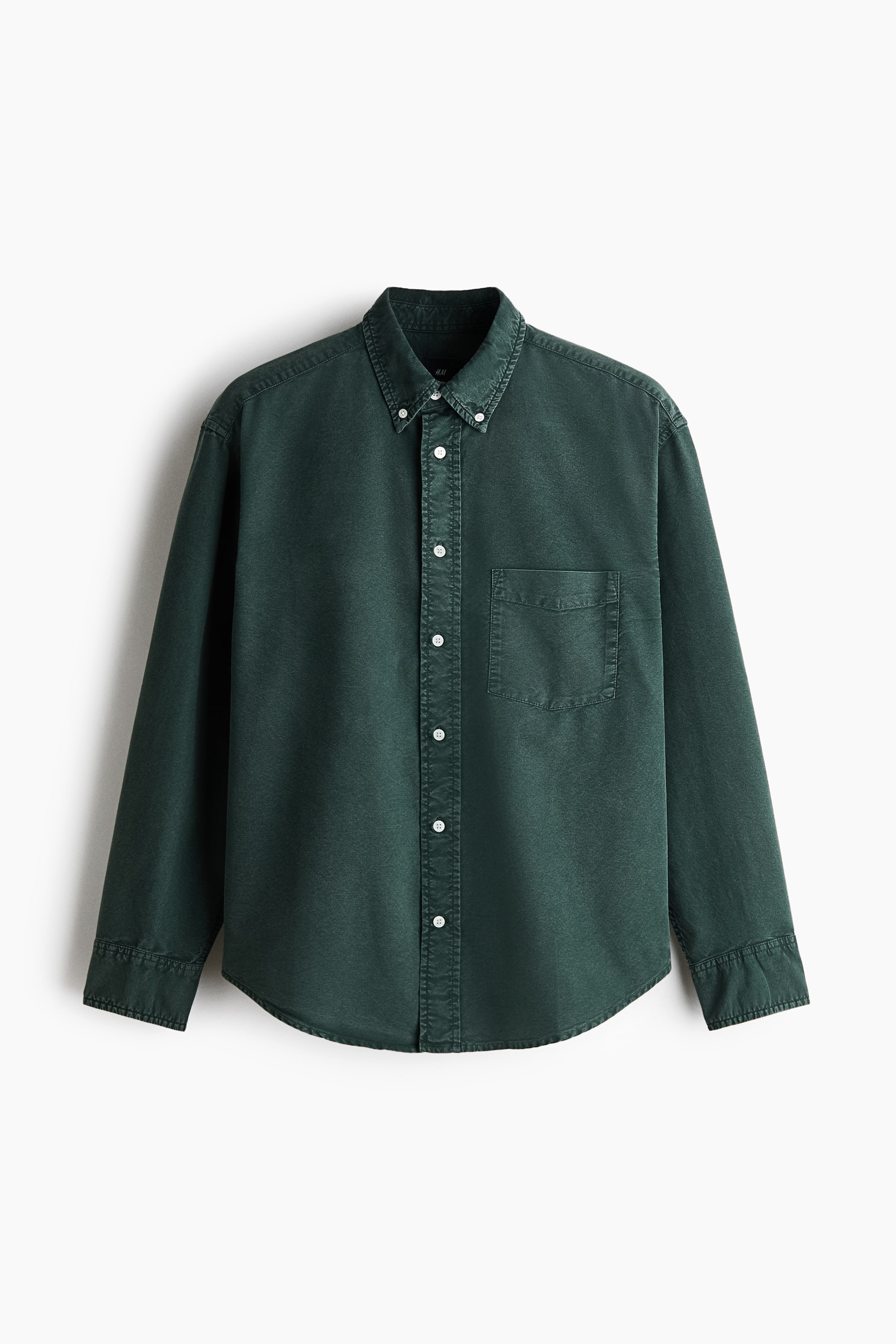 View larger image: A dark green Oxford cotton shirt is hanging facing forward, showcasing a relaxed fit with a button-down collar and a central button placket. The shirt features a single open chest pocket on the left, long sleeves with buttoned cuffs, and a gently rounded hem.