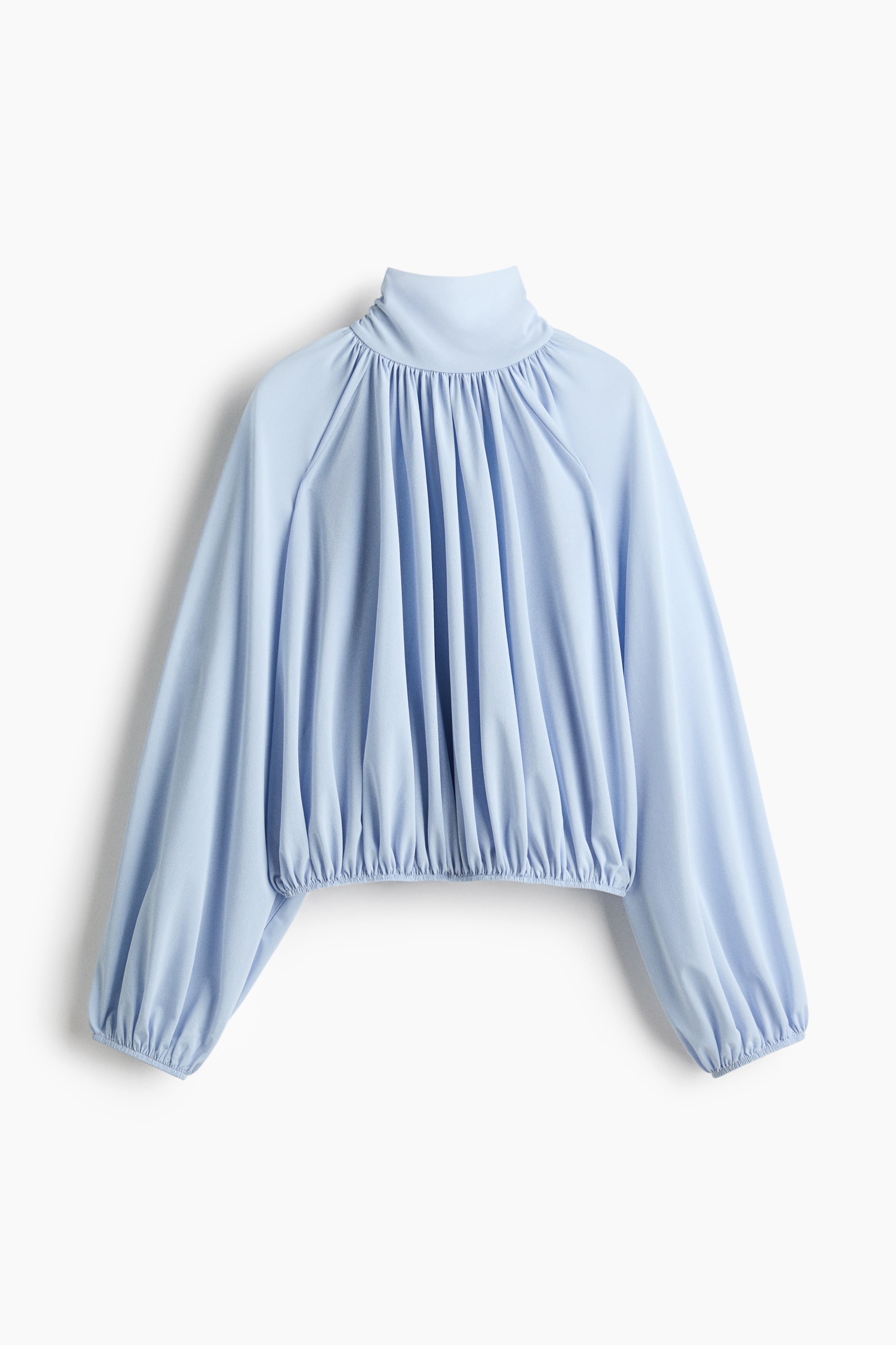 View larger image: A light blue top is shown facing forward, featuring a high, gathered mock neck and long, voluminous raglan sleeves with elasticated cuffs. The top is also gathered at the bottom hem, creating a cropped, billowy silhouette.