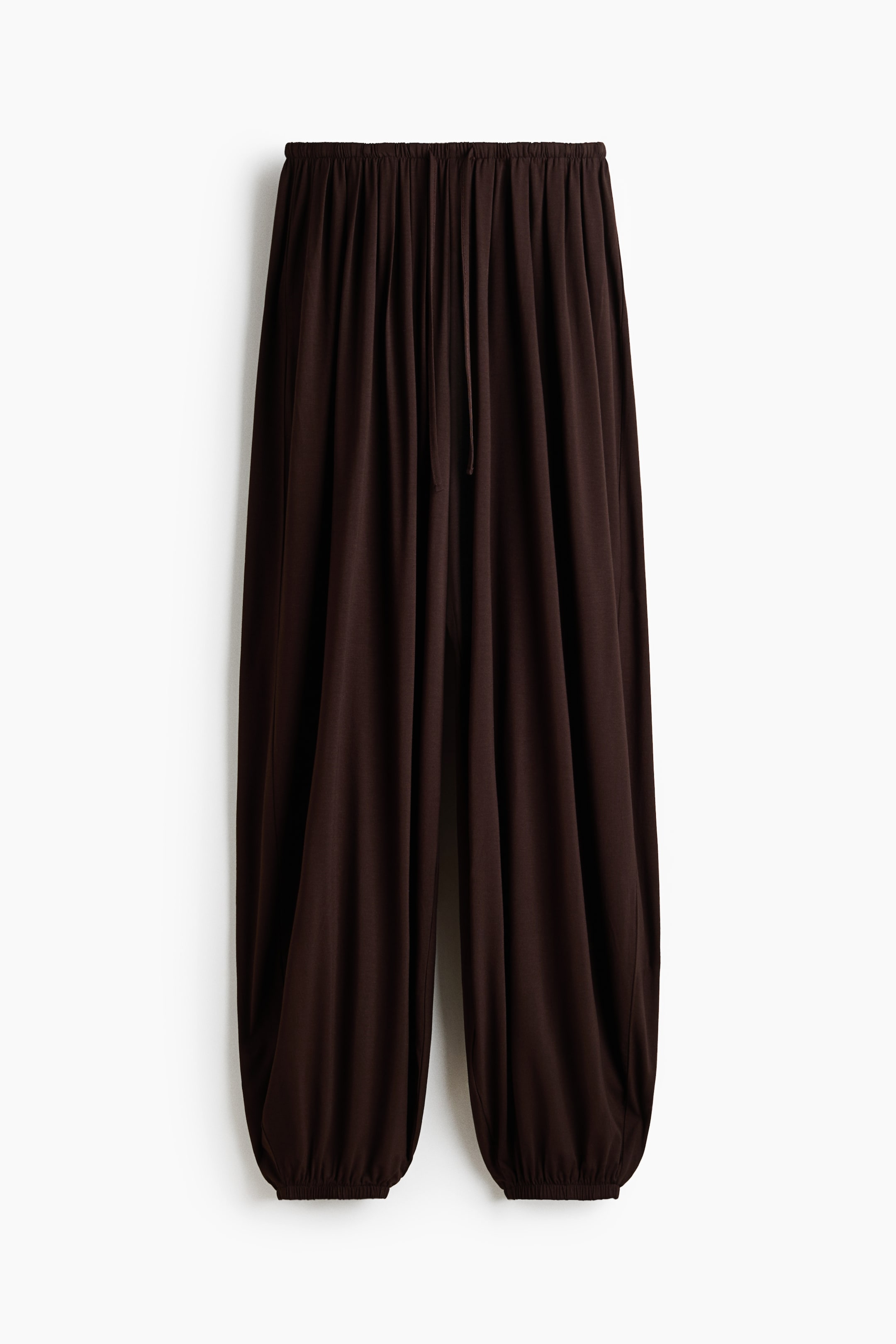 View larger image: Dark brown pants showcase a relaxed, flowing fit with an elastic drawstring waistband and gathered elastic cuffs at the ankles.