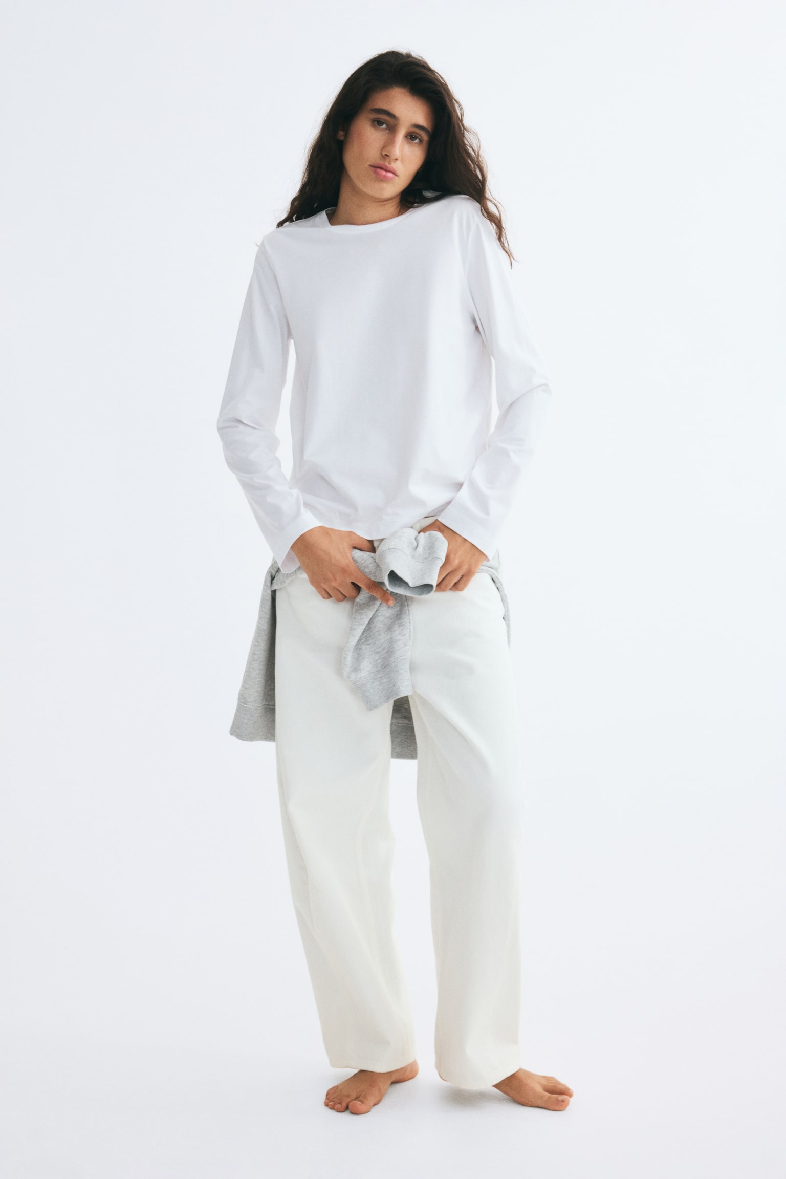 A white cotton jersey top is shown from the front, featuring a round, rib-trimmed neckline and long, straight sleeves. - 1