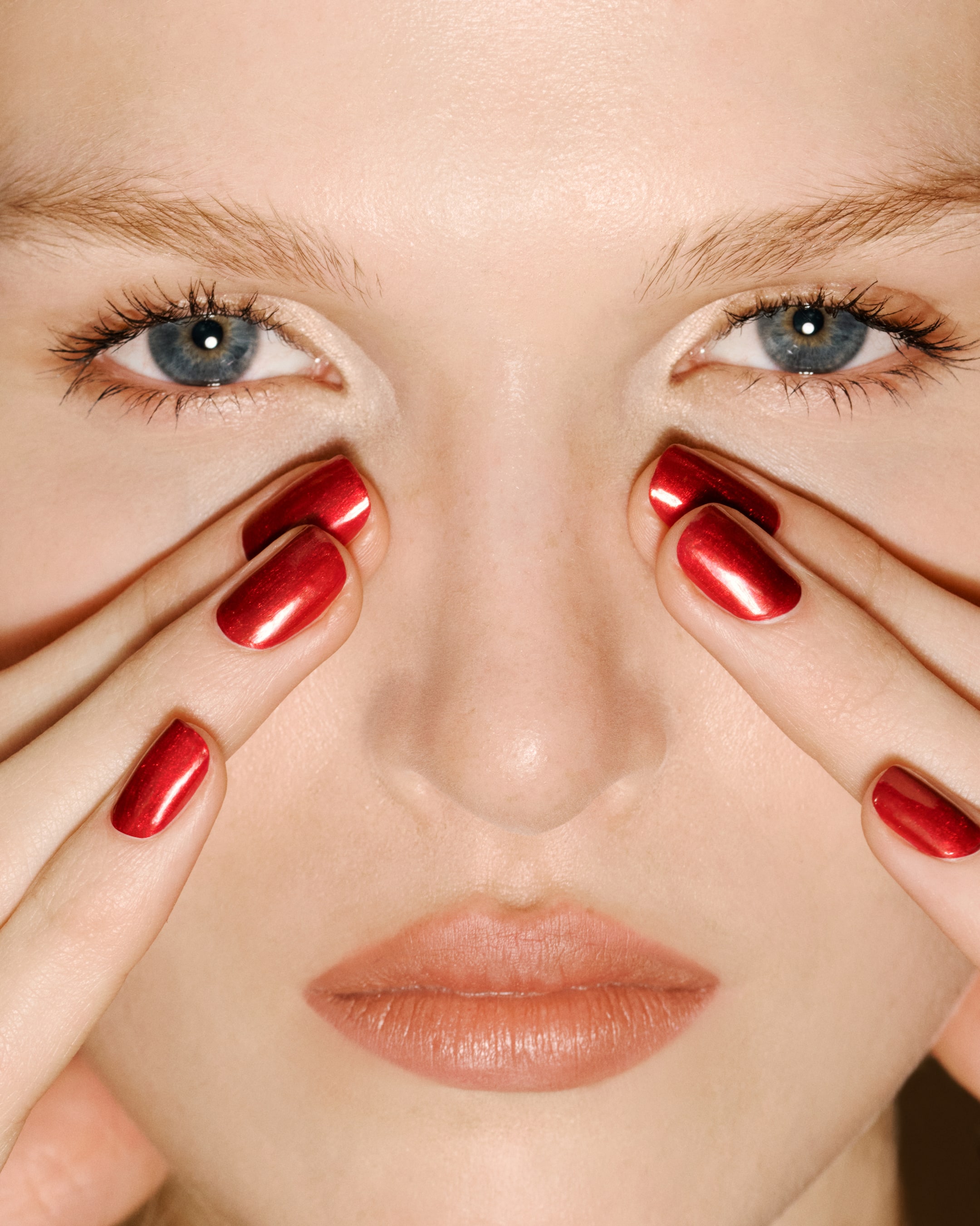 Agrandir l'image: Le vernis à ongles rouge métallisé scintillant est présenté sur des ongles manucurés, qui encadrent le visage d’un mannequin afin de mettre en valeur sa finition ultra brillante et réfléchissante ainsi que sa couvrance riche.