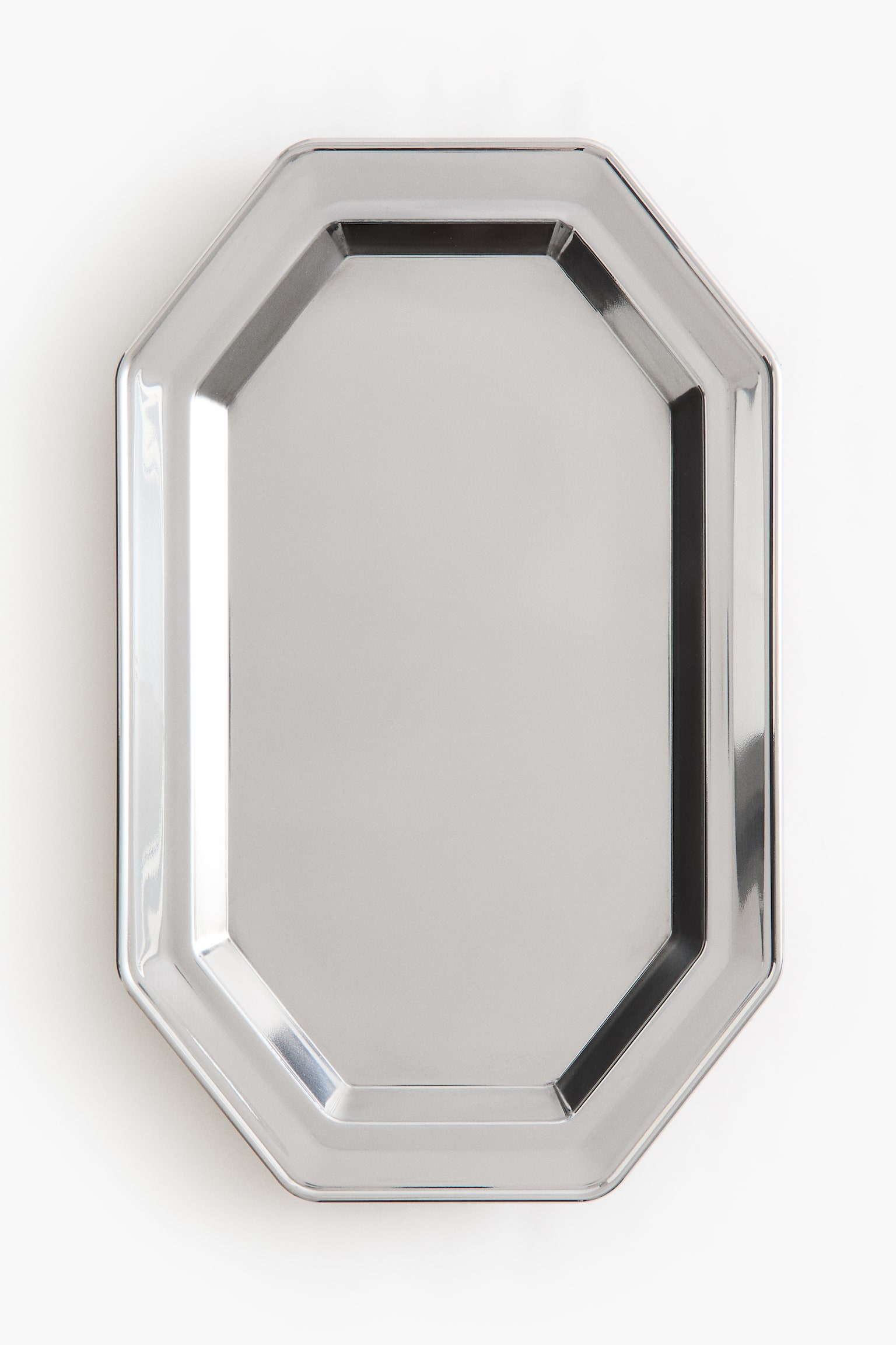 A silver-coloured metallic tray is showing a front-facing, elongated octagonal shape with a highly polished, reflective finish. The tray features a raised, multi-angled rim surrounding a flat, smooth central surface.