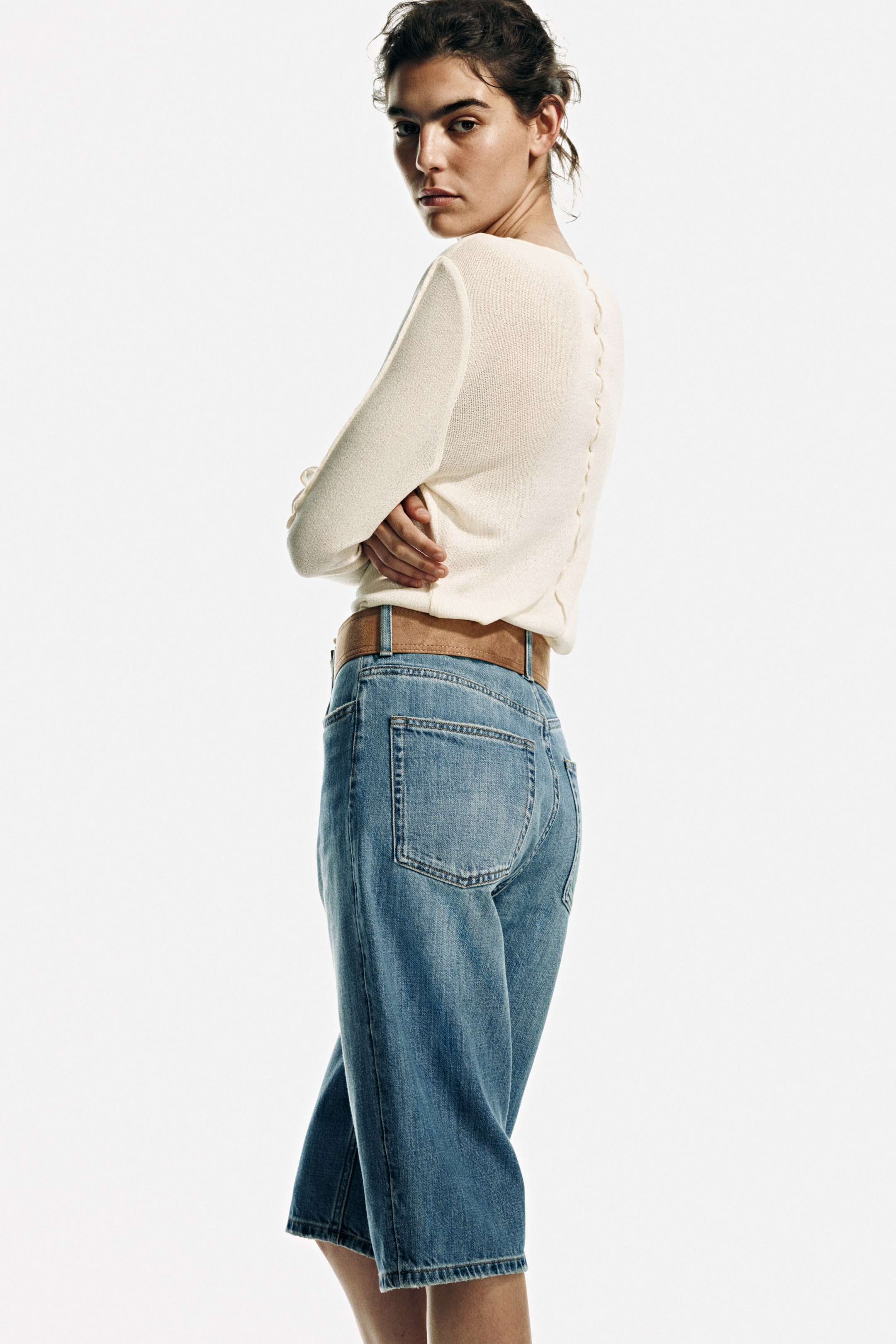 View larger image: An off-white knit top featuring a row of small buttons along the back is styled with light blue wash wide-leg denim culottes, cinched at the waist with a tan belt.