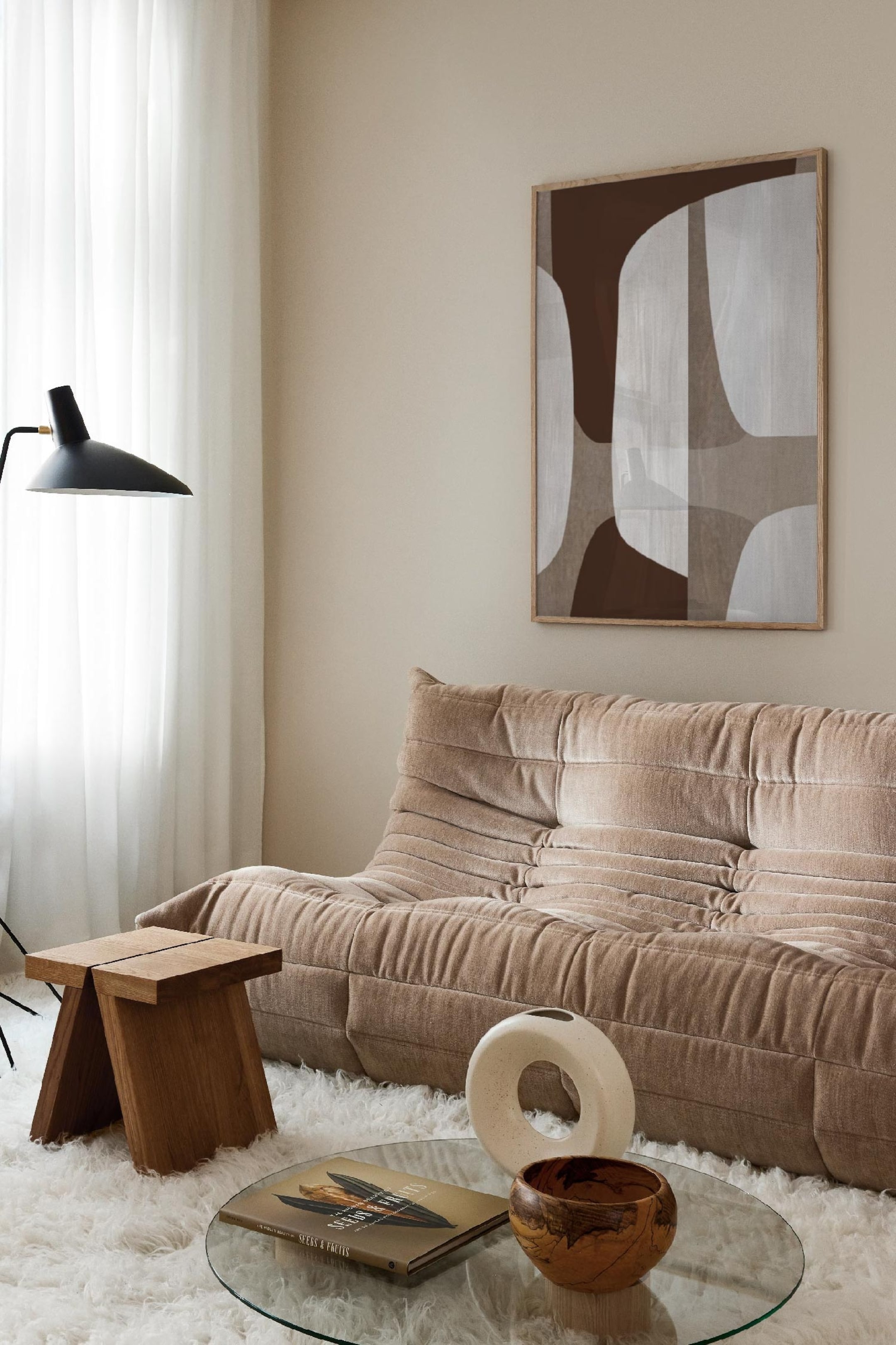 Agrandir l'image: Le canapé est une pièce basse, de couleur taupe clair, orientée légèrement vers la droite, avec un tissu doux à fines côtes verticales. Il présente un design profondément plissé et matelassé sur tout le dossier et l’assise.