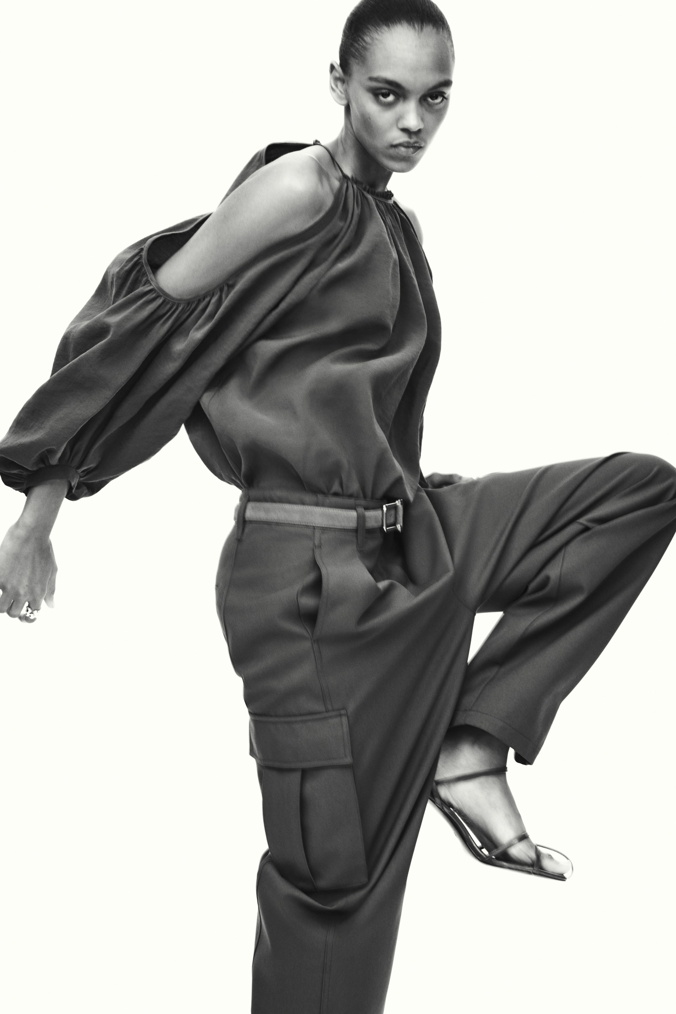 Näytä suurempi kuva: Mallilla on yllään löysät cargo-housut, joissa on korkea vyötärö ja vyöllä kiristetty istuvuus. Housuissa on sivusaumataskut, etulaskokset ja paljetasku läpässä tynnyrijalassa.