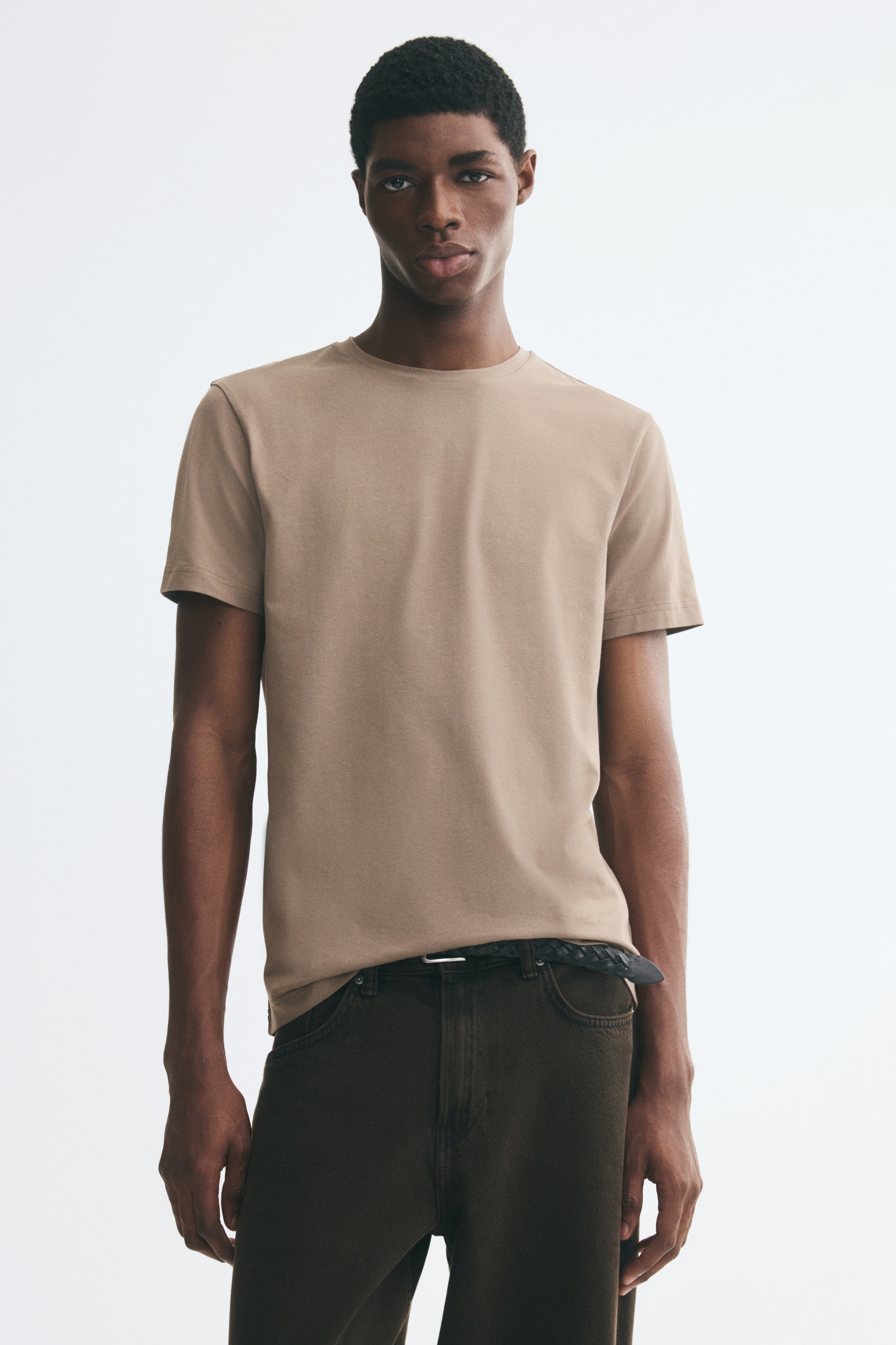A brown crew-neck T-shirt is facing front, featuring short sleeves and a straight, double-stitched hem. The solid-coloured garment displays a smooth texture and a regular fit.