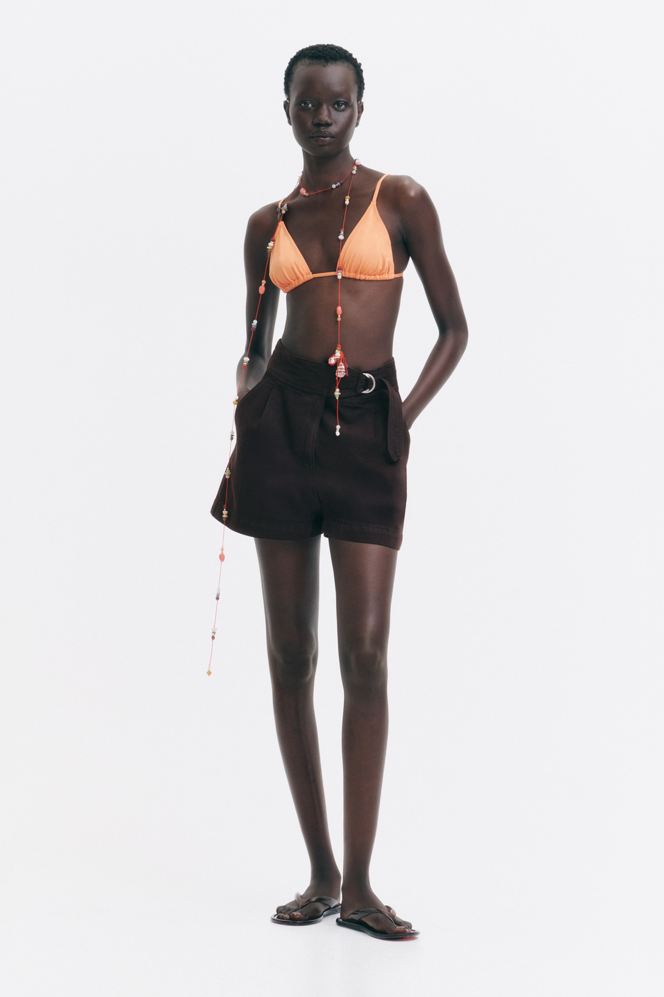 View larger image: Dark brown high-waisted shorts feature a pleated front and side pockets. A matching fabric belt with a silver-tone D-ring buckle cinches the waist, and the shorts extend to mid-thigh length from a front view.
