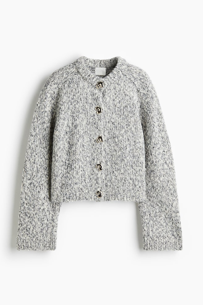 A grey and white speckled knit cardigan is displayed from the front, featuring a crew neck and five gold-toned buttons down its center. It is designed with long raglan sleeves and is finished with ribbed cuffs and a ribbed hem, presenting a cropped silhouette. - 1