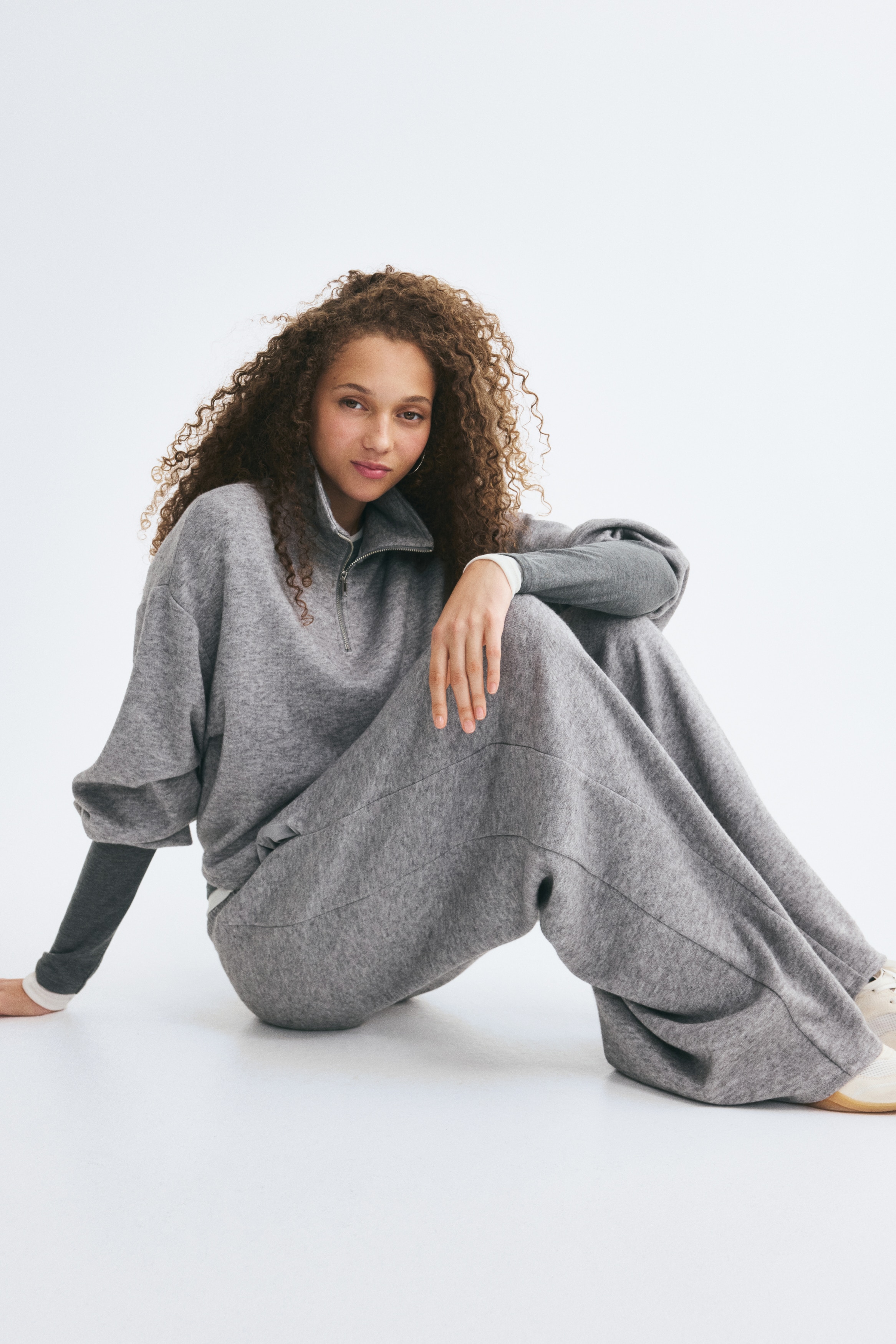 A grey marled knit jumpsuit is hanging facing the front, featuring a high collar with a half-zip closure, long balloon sleeves with gathered cuffs, and a cropped overlay top over matching wide-leg pants.