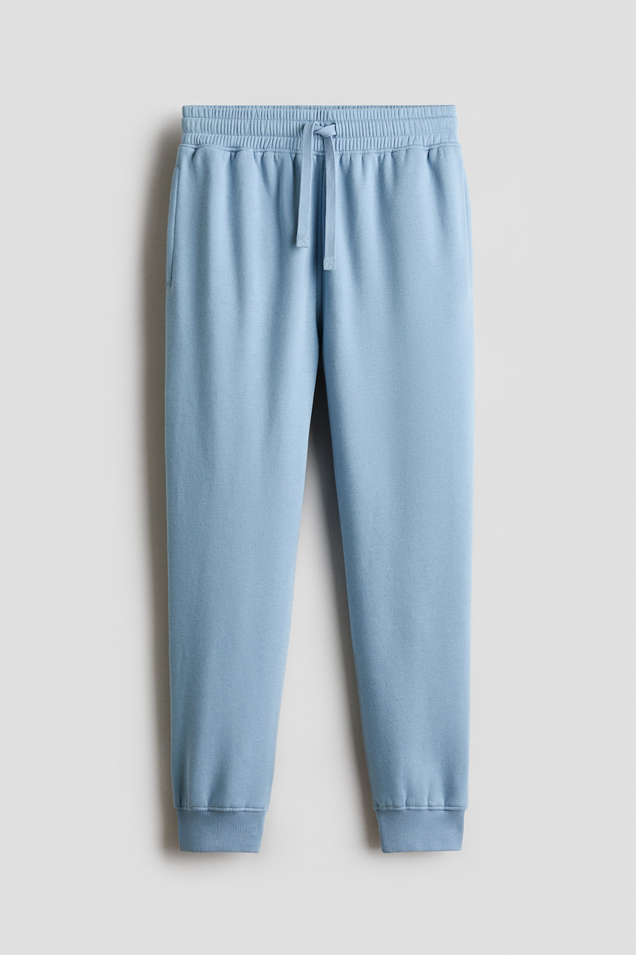 Agrandir l'image: Un pantalon de jogging bleu clair en molleton est présenté de face, avec une taille élastiquée à cordon de serrage noué. Le pantalon de jogging est doté de poches latérales, de jambes fuselées et de poignets côtelés.