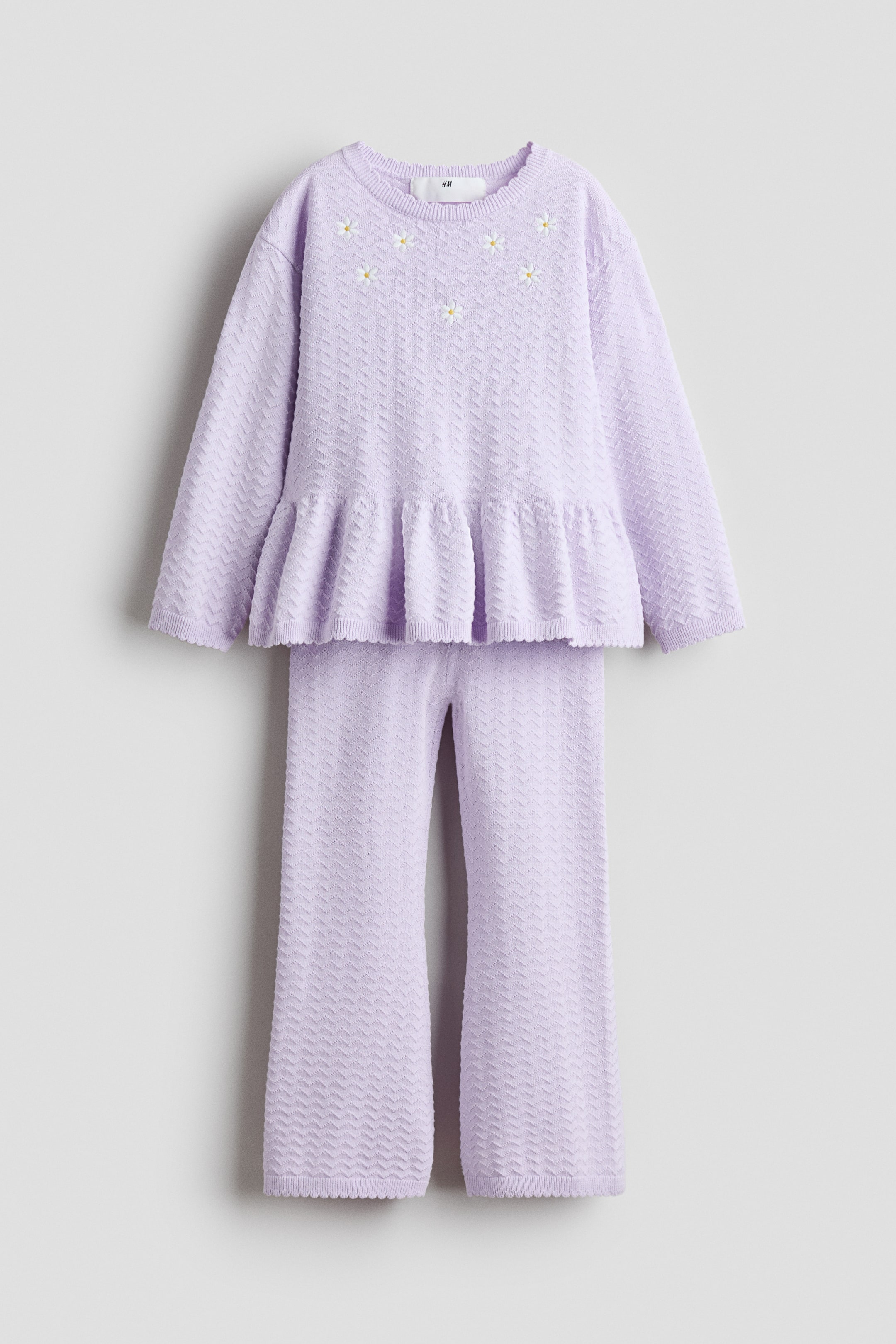 View larger image: The long-sleeved top is featuring a round neck, daisy embroidery around the neckline, and a ruffled peplum hem, while the wide-leg pants are showcasing a matching chevron knit pattern.