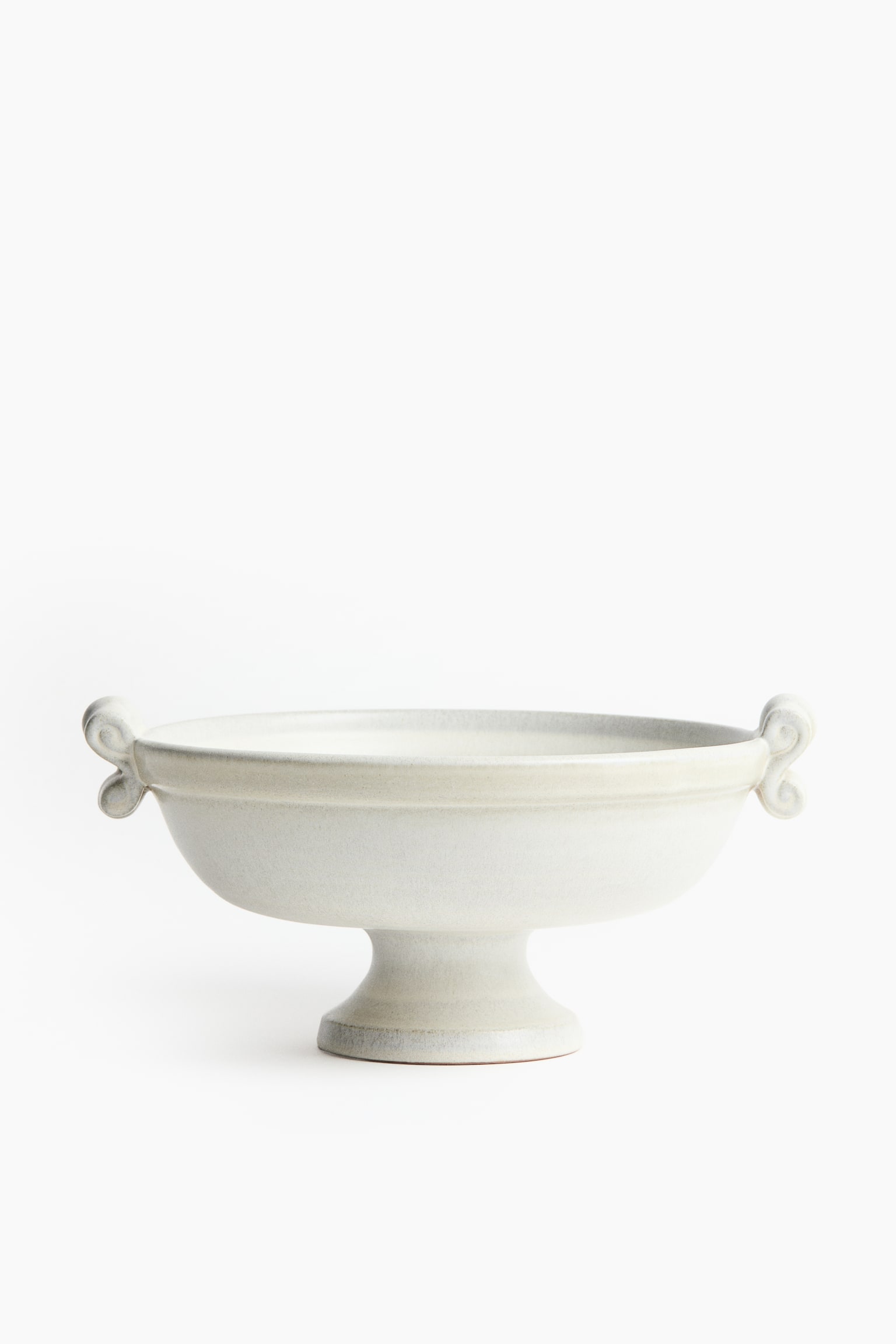 Un bol sur piédestal en céramique blanc cassé est présenté de face, doté dâun large bassin peu profond soutenu par un pied évasé. Le bol arbore des anses décoratives en forme de volute sur les côtés opposés et un bourrelet horizontal en relief courant tout autour du bord supérieur. - 1