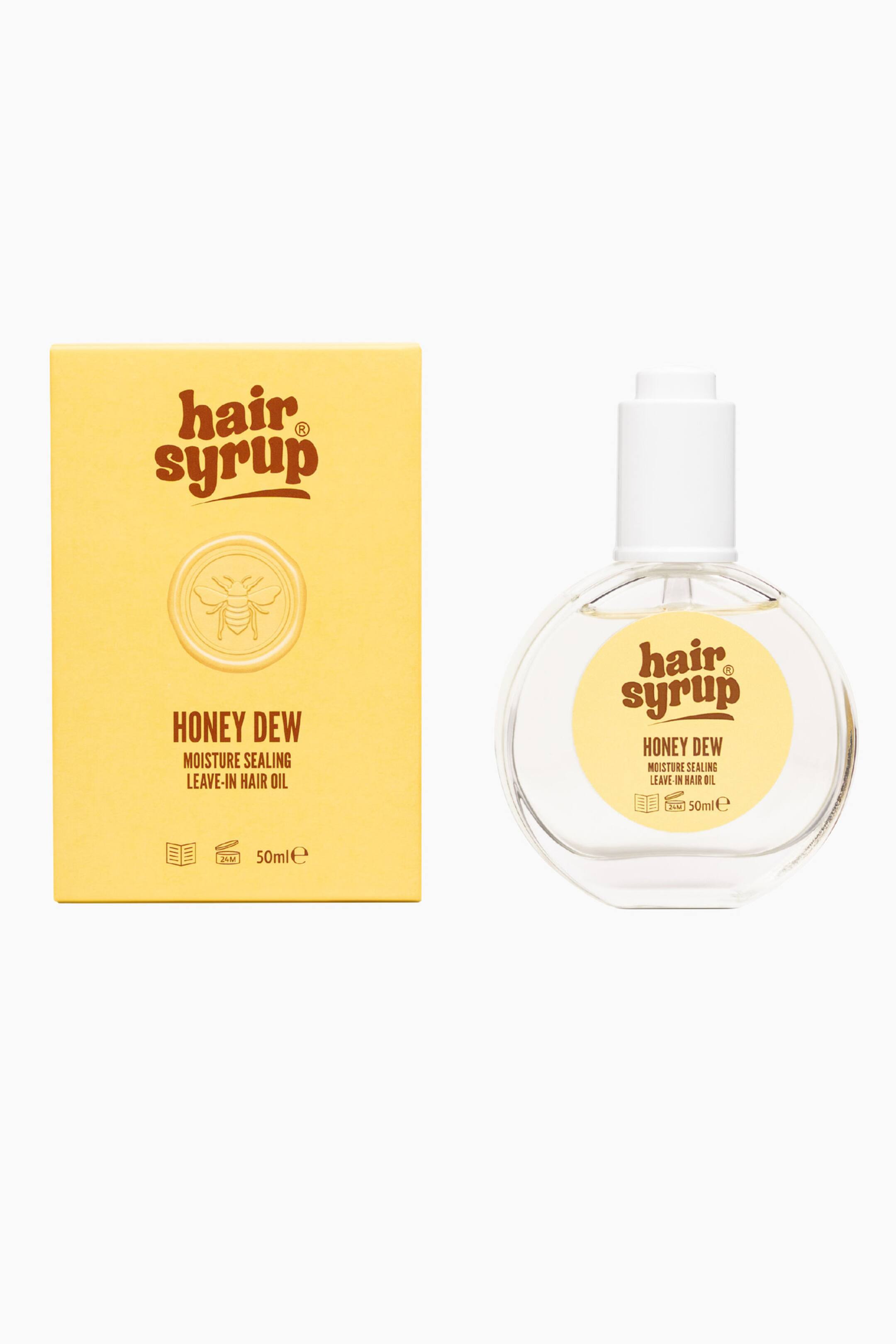 Visa större bild: Hair Syrup Honey Dew leave-in-hårolja står upprätt och visar en gul rektangulär ytterkartong bredvid en rund, genomskinlig glasflaska. Kartongen visar brunt varumärkestryck med ett bitemblem, medan flaskan har en matchande rund gul etikett och är försedd med en vit pumphatt.