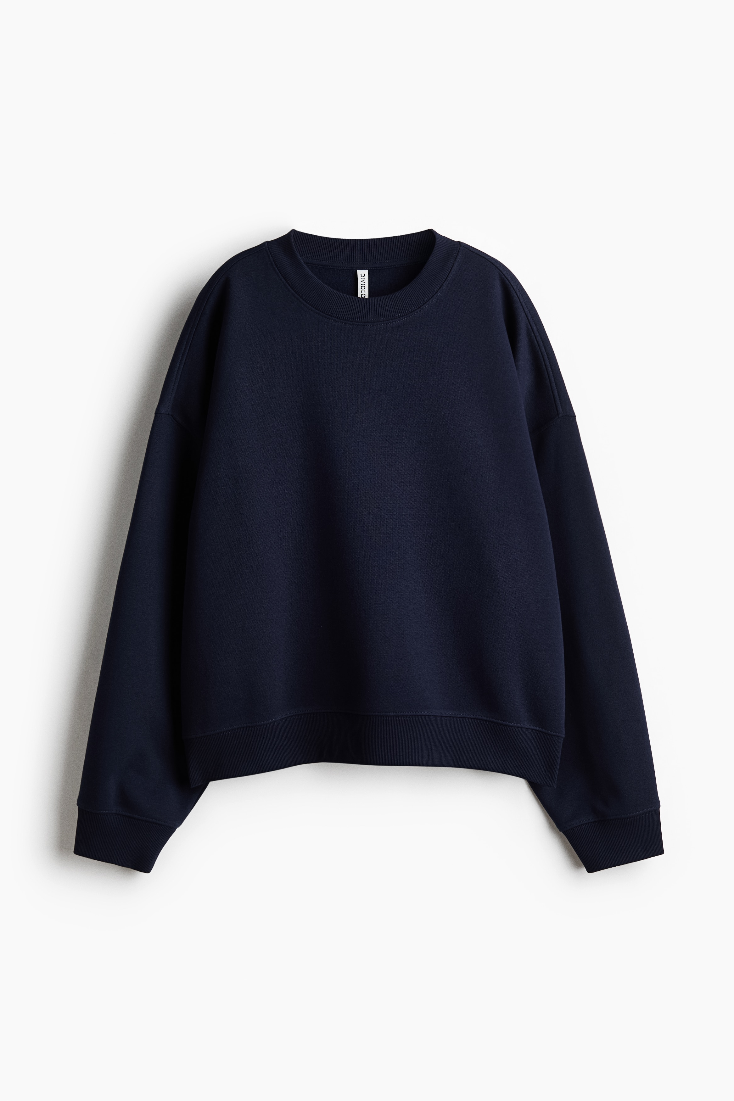 The model is wearing an oversized navy blue sweatshirt featuring a round ribbed neckline, dropped shoulders, and ribbed cuffs. The sweatshirt is layered over a striped light blue shirt and paired with wide-leg, light-wash jeans.