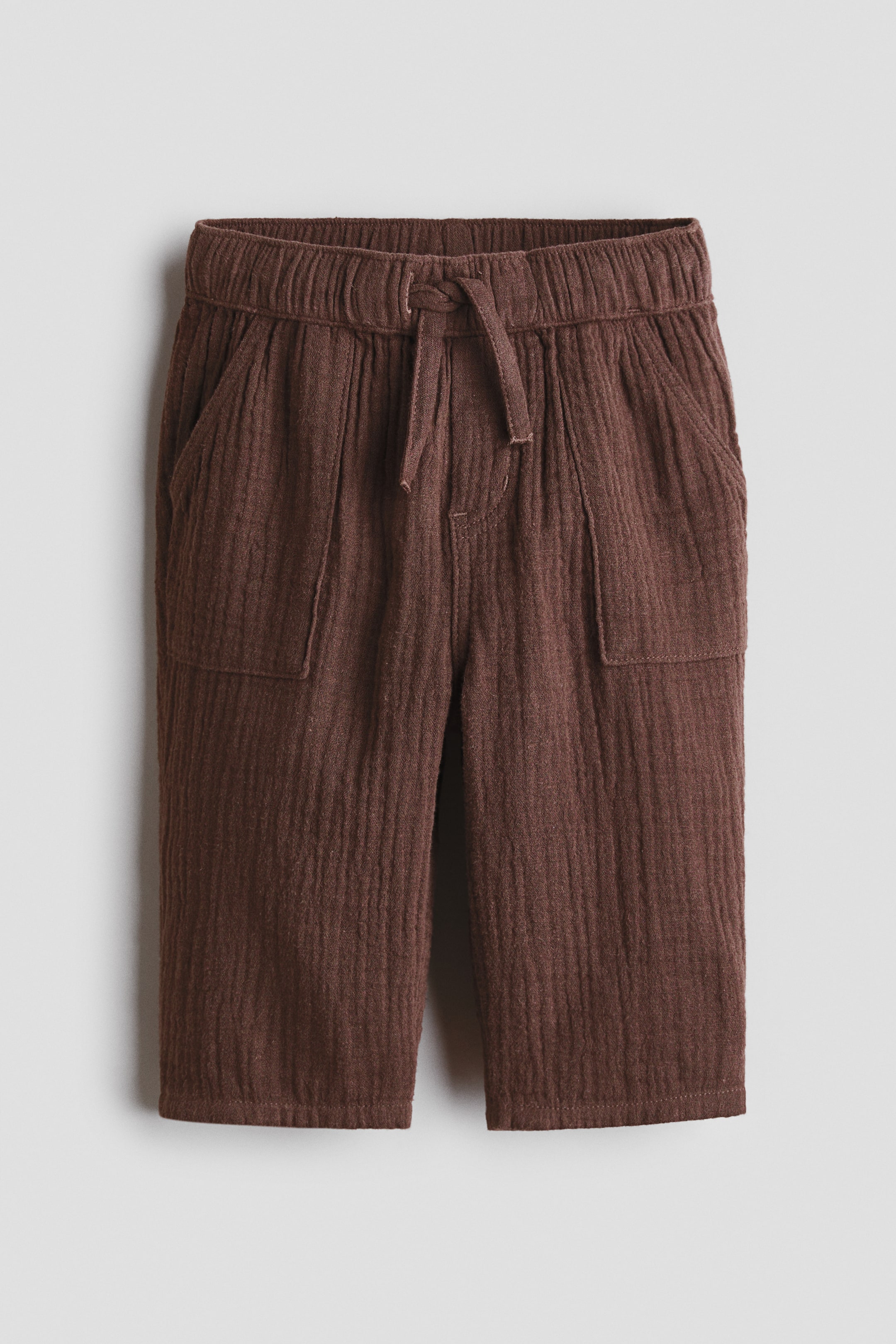 Ampliar la imagen: Pantalones marrones con textura arrugada, cintura elástica con cordón ajustable y lazo, bragueta falsa y dos bolsillos delanteros de parche. Las piernas se estrechan hacia abajo.