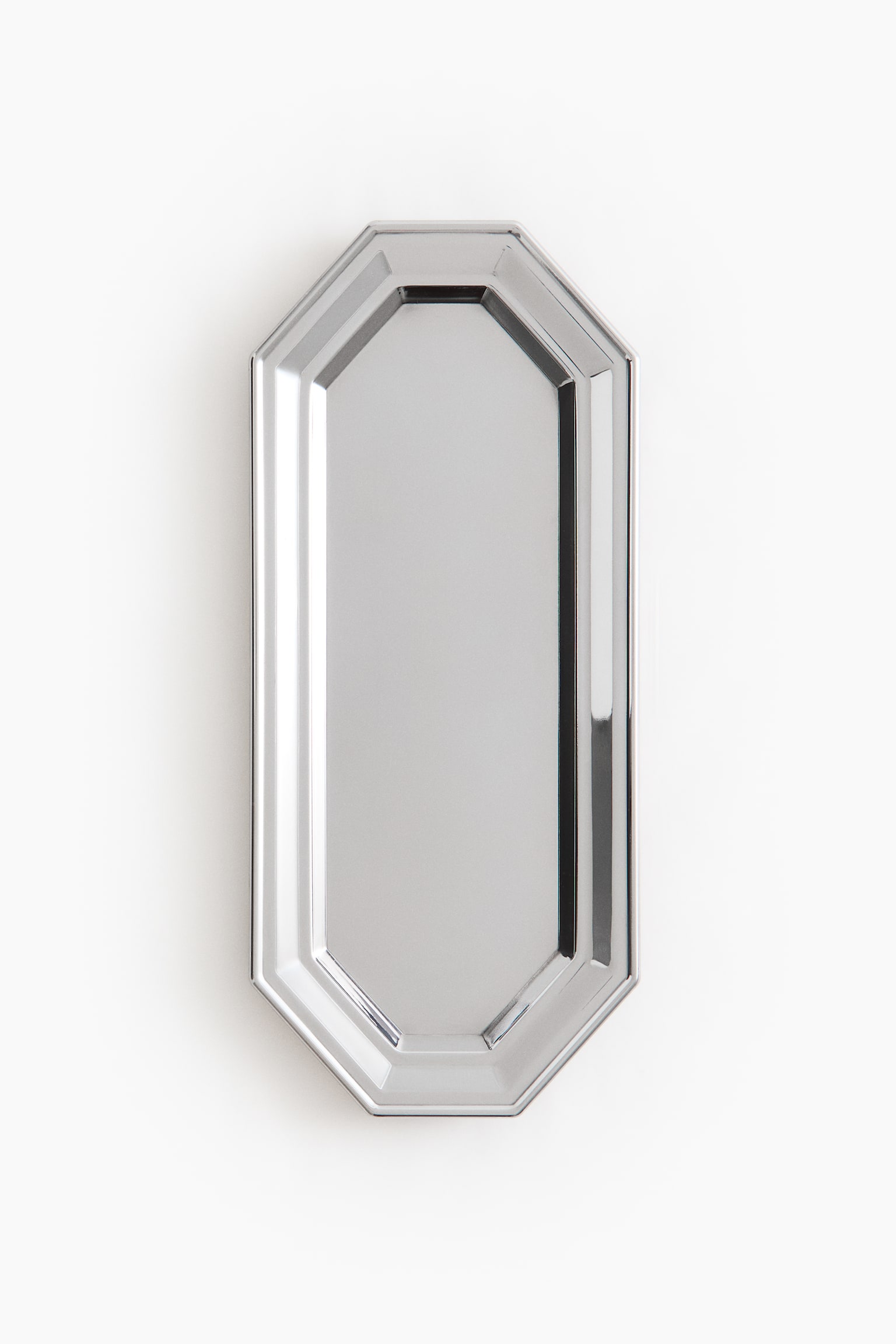 Un plateau octogonal allongÃ© est prÃ©sentÃ© de face, mettant en valeur une finition mÃ©tallique ton argent hautement polie, avec une surface rÃ©flÃ©chissante de type miroir. Le plateau prÃ©sente un centre plat et en retrait, entourÃ© dâun rebord surÃ©levÃ© Ã  paliers aux arÃªtes nettes et angulaires.